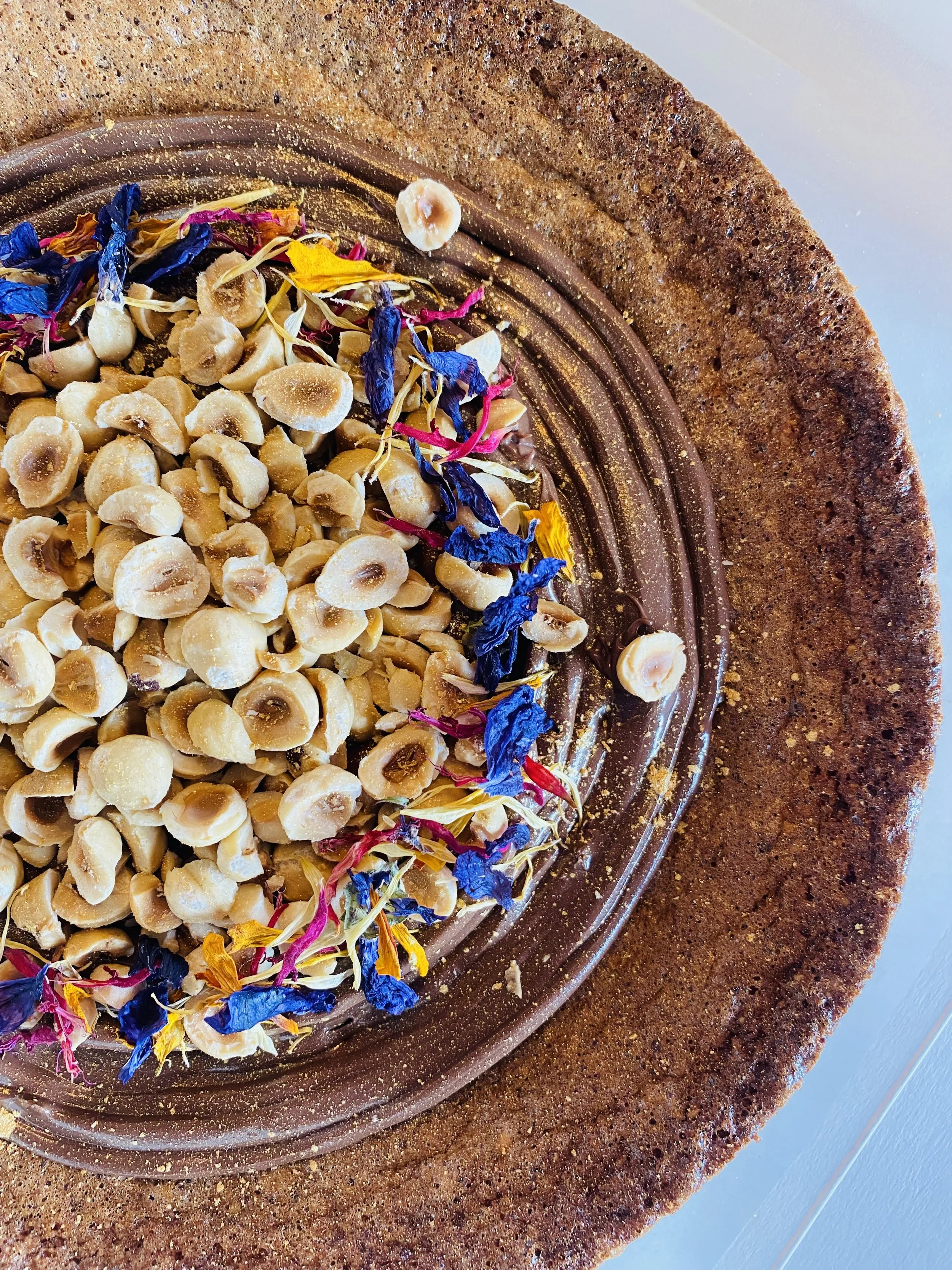 Gâteau au chocolat décoré avec des fleurs séchées et des noisettes, placé sur une table en bois.