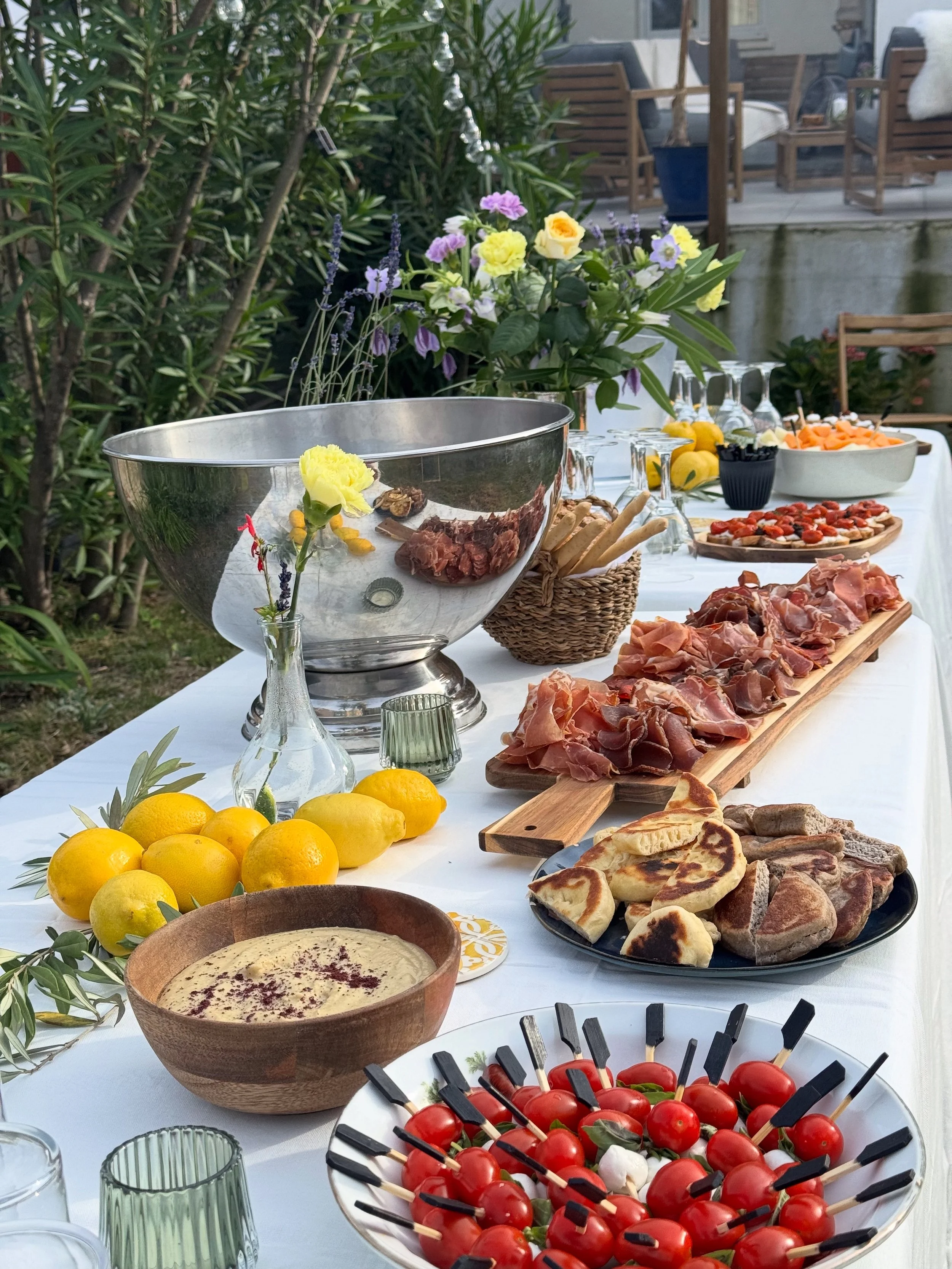 Un buffet d'été avec des fruits, des viandes, des légumes, et des boissons, décoré de fleurs et de citrons, en plein air.