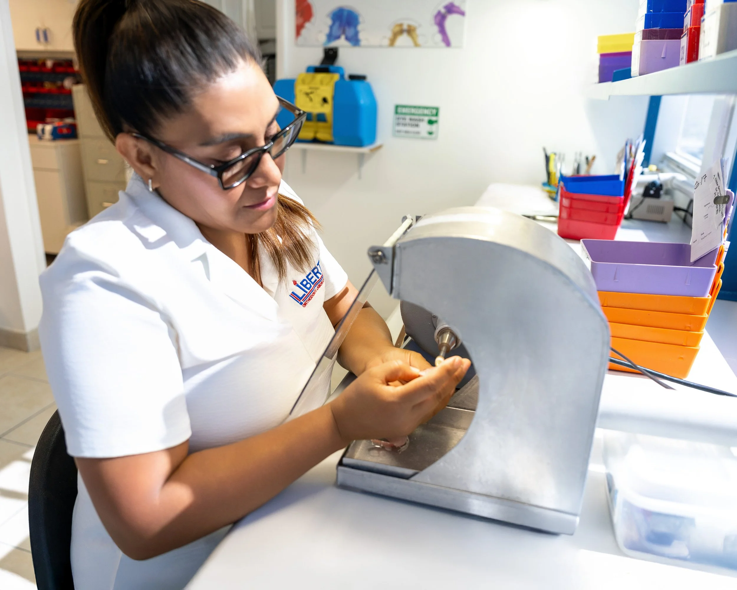 A woman wearing glasses and a white shirt working with medical equipment at a counter in a clinical setting.