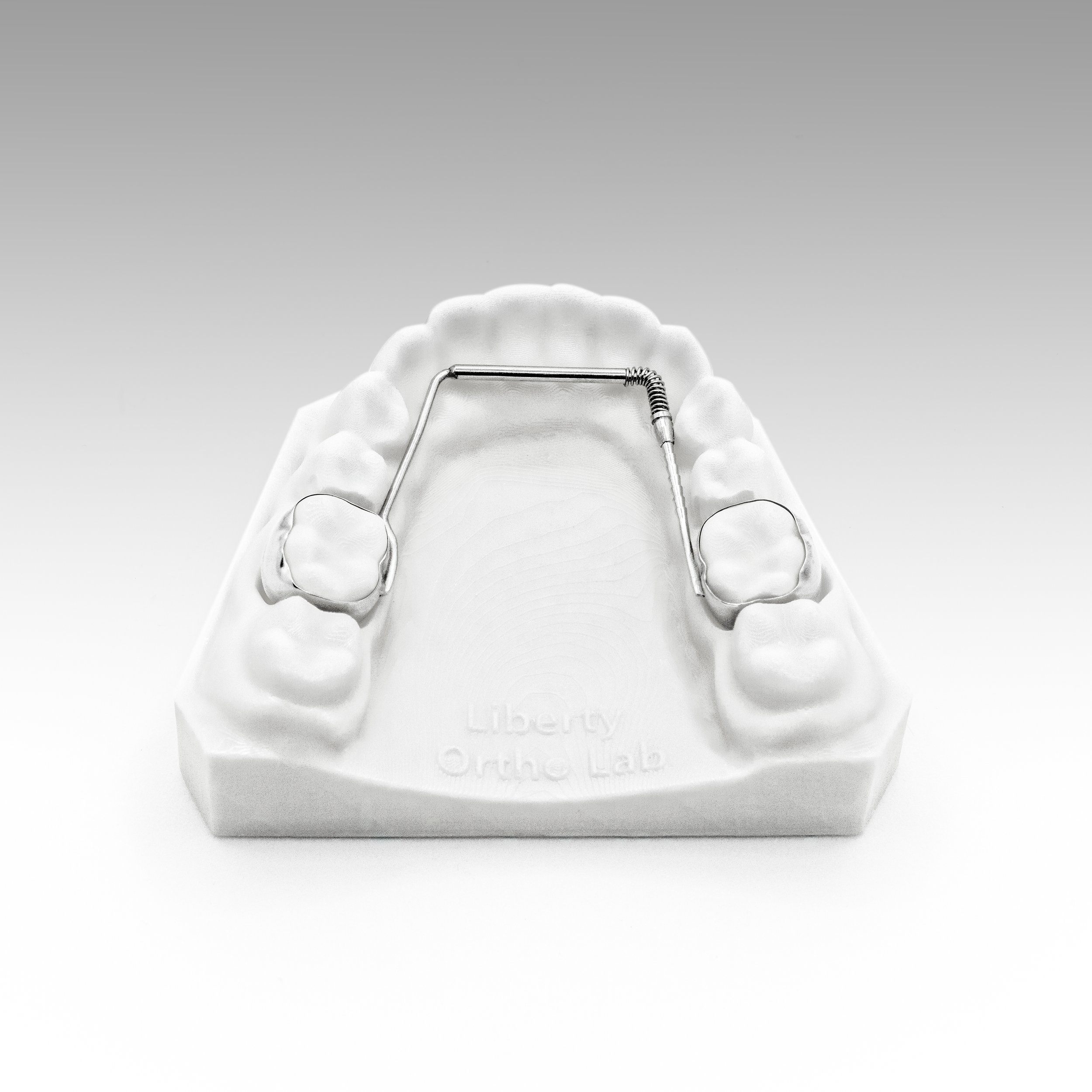 A white dental mold of the upper teeth with a dental panoramic x-ray and dental tools placed on top, including a dental mirror and a dental explorer, against a gray gradient background.