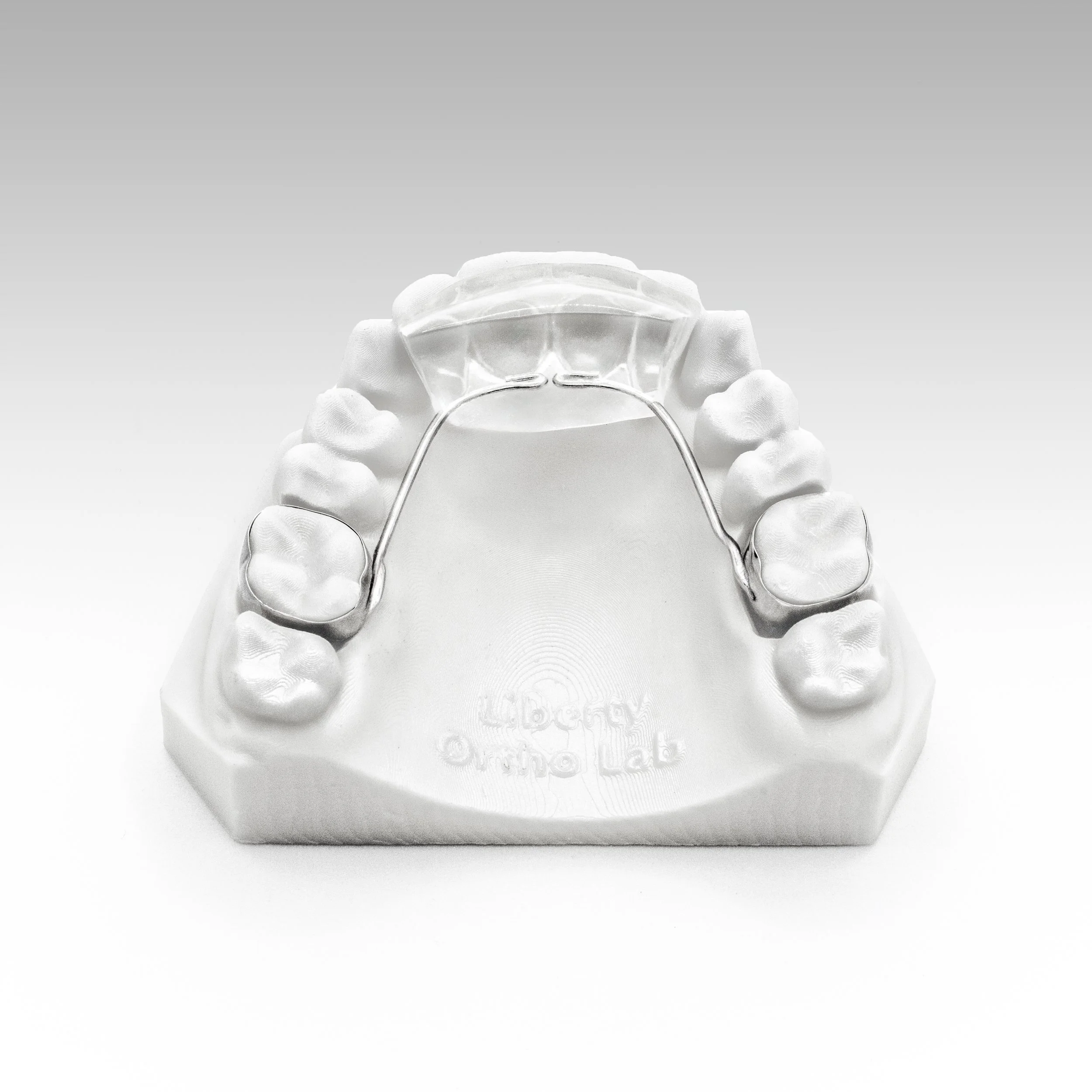 Close-up of a clear dental aligner held by gloved hands against a light gray background.