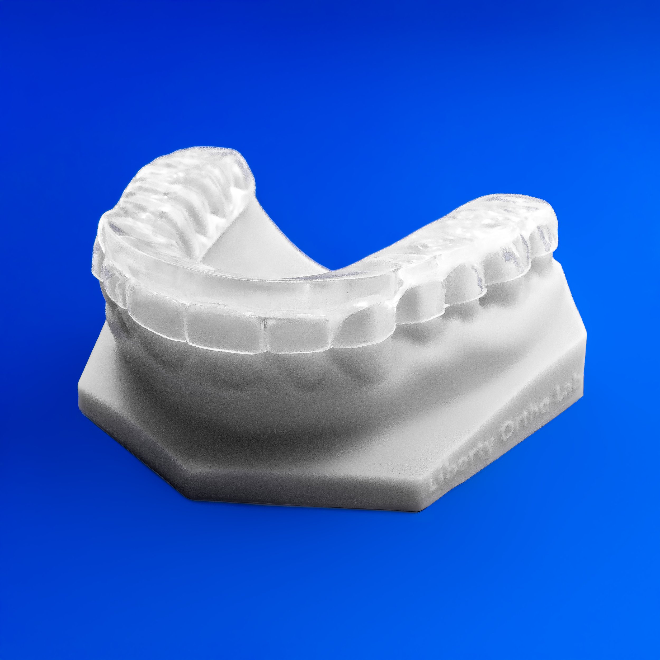 Close-up of a clear dental aligner resting on a white surface against a blue background.