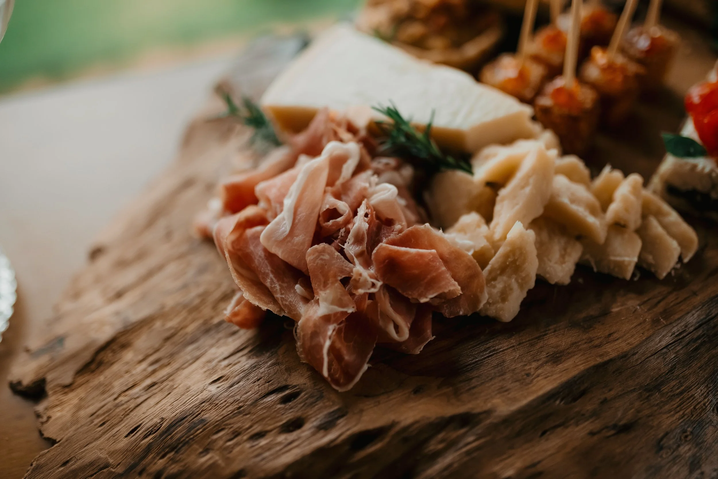 Close-up of assorted cheeses and cured meats on a rustic wooden serving board, garnished with a sprig of fresh thyme.