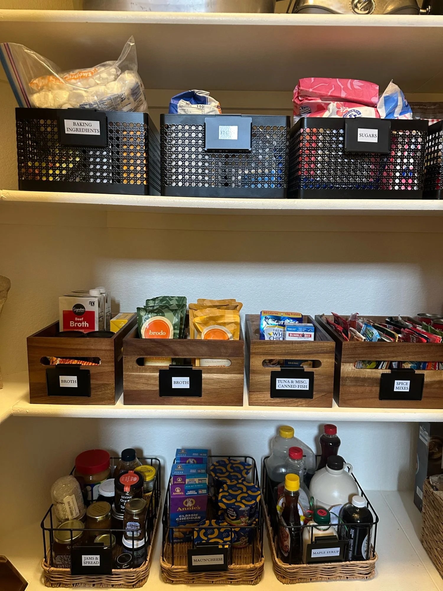Pantry shelves organized with labeled bins for snacks, condiments, canned goods, and food storage. 