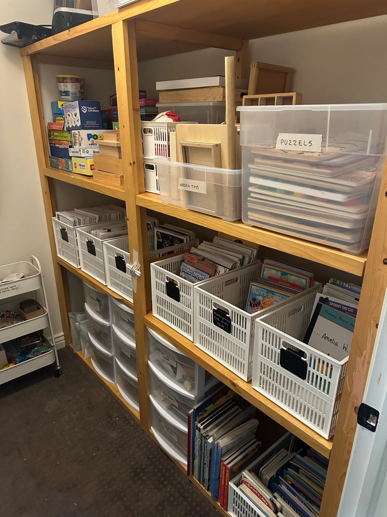 Wooden shelving organized with labeled bins, books, and craft supplies for easy access. 
