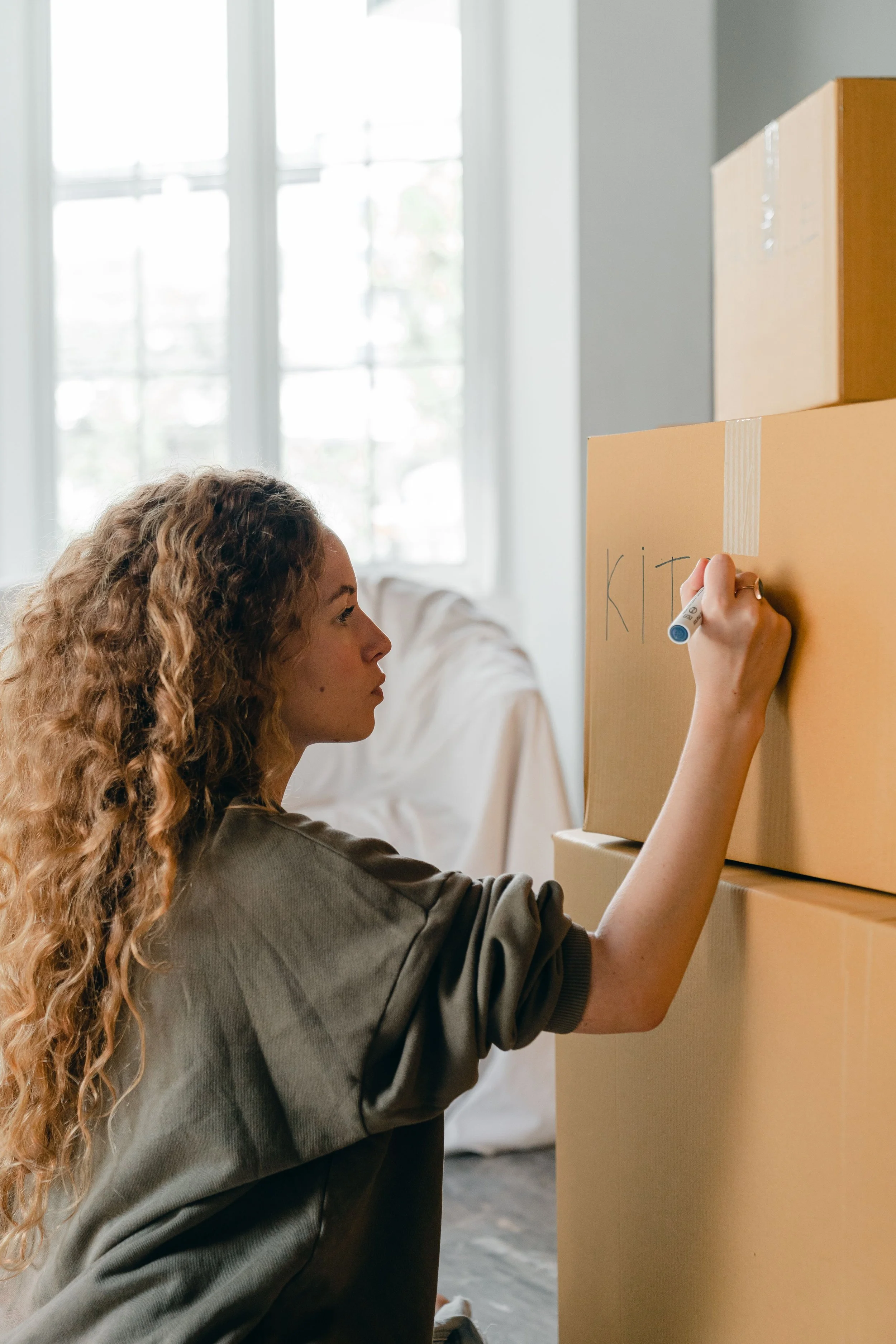 Woman preparing for a move by labeling cardboard boxes for easy unpacking.