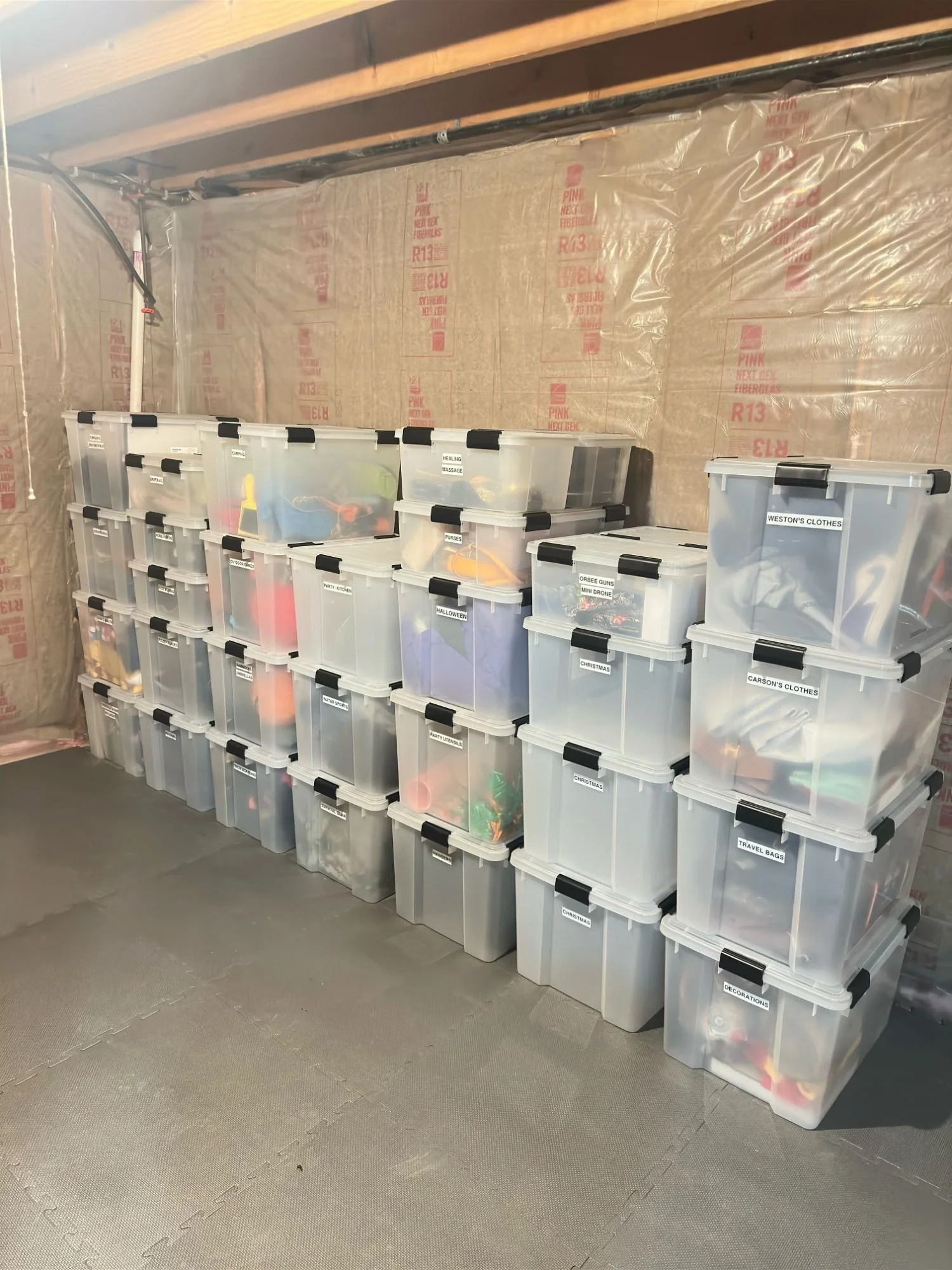 Clear storage bins neatly organized and labeled in a basement storage room. 