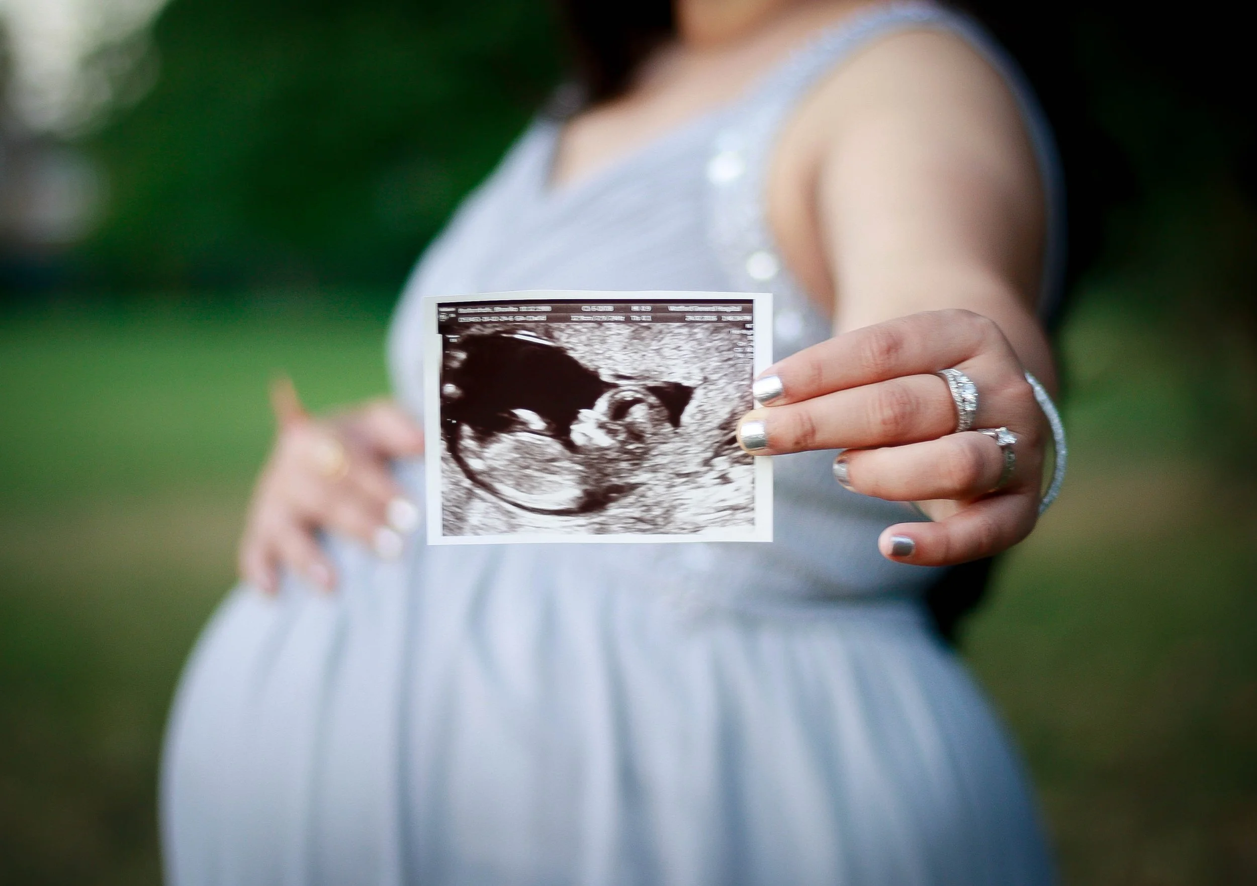 rosecroft photography portraits Pregnant woman smiling and holding her ultrasound scan towards the camera during a maternity portrait session