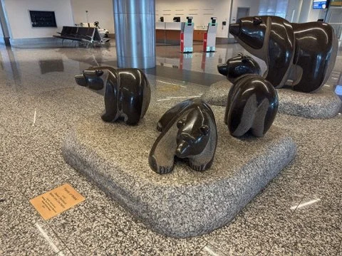 Stone sculptures of bears and a dog displayed on a granite platform at an airport.