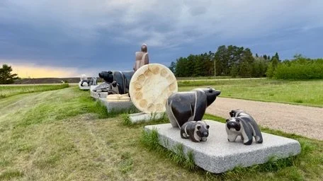 Outdoor sculpture featuring several dog statues on a grassy area with a cloudy sky and trees in the background.