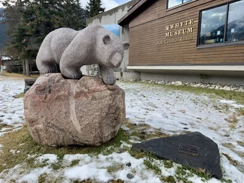 Granite bear sculpture on rock outside of a museum building with snow on the ground.