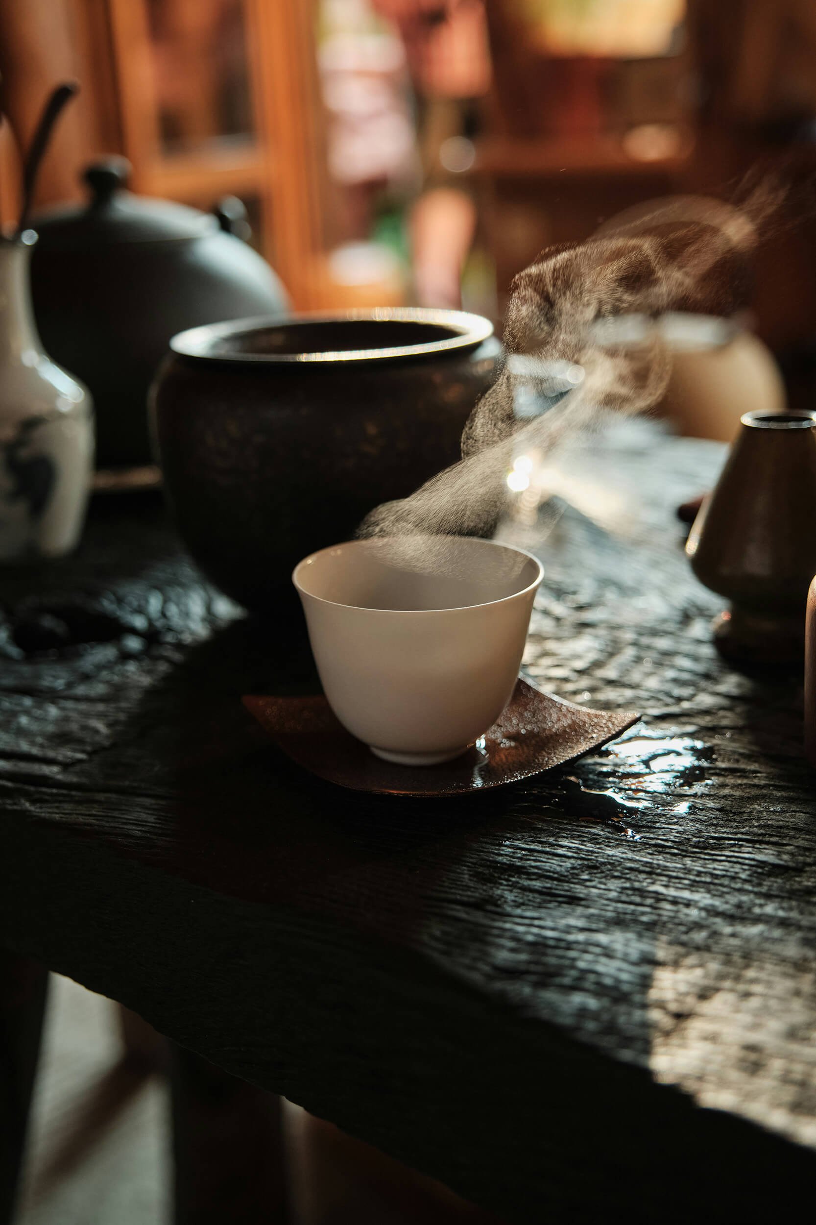 Steam rising from a small white teacup on a dark, textured wooden table as part of a TCM appointment at New Heights Acupuncture and Chinese Medicine in Houston, Texas.