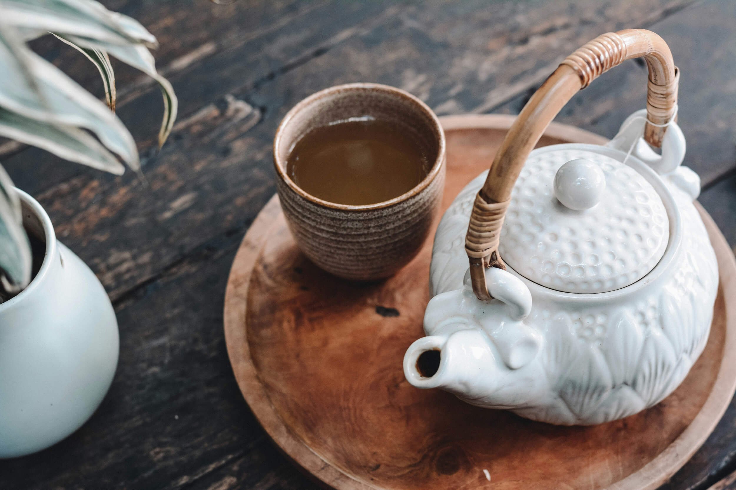 A teapot and a cup of tea on a wooden tray representing Chinese herbal medicine.
