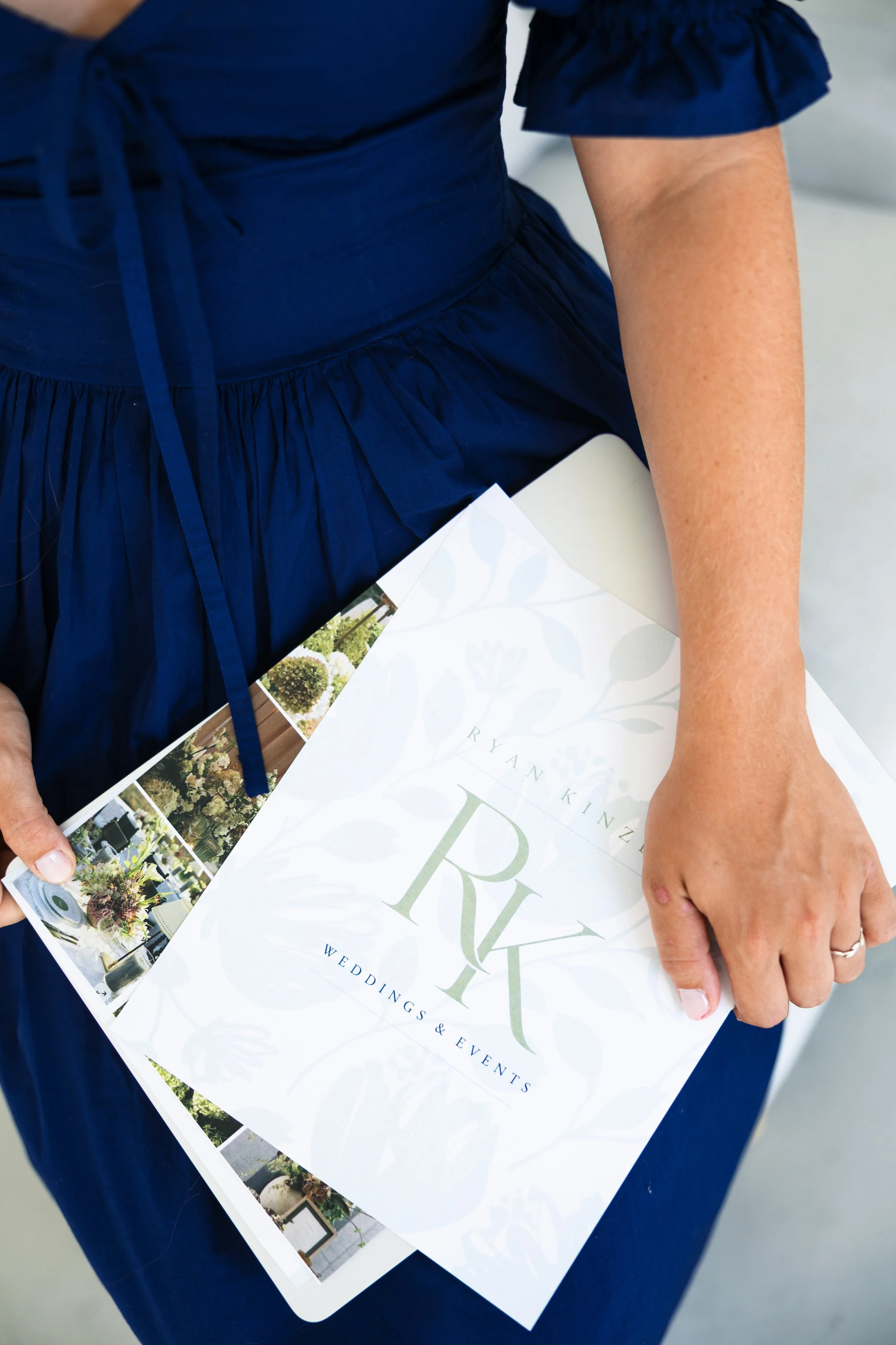 A person dressed in a navy blue dress holding a wedding and events brochure with garden pictures.