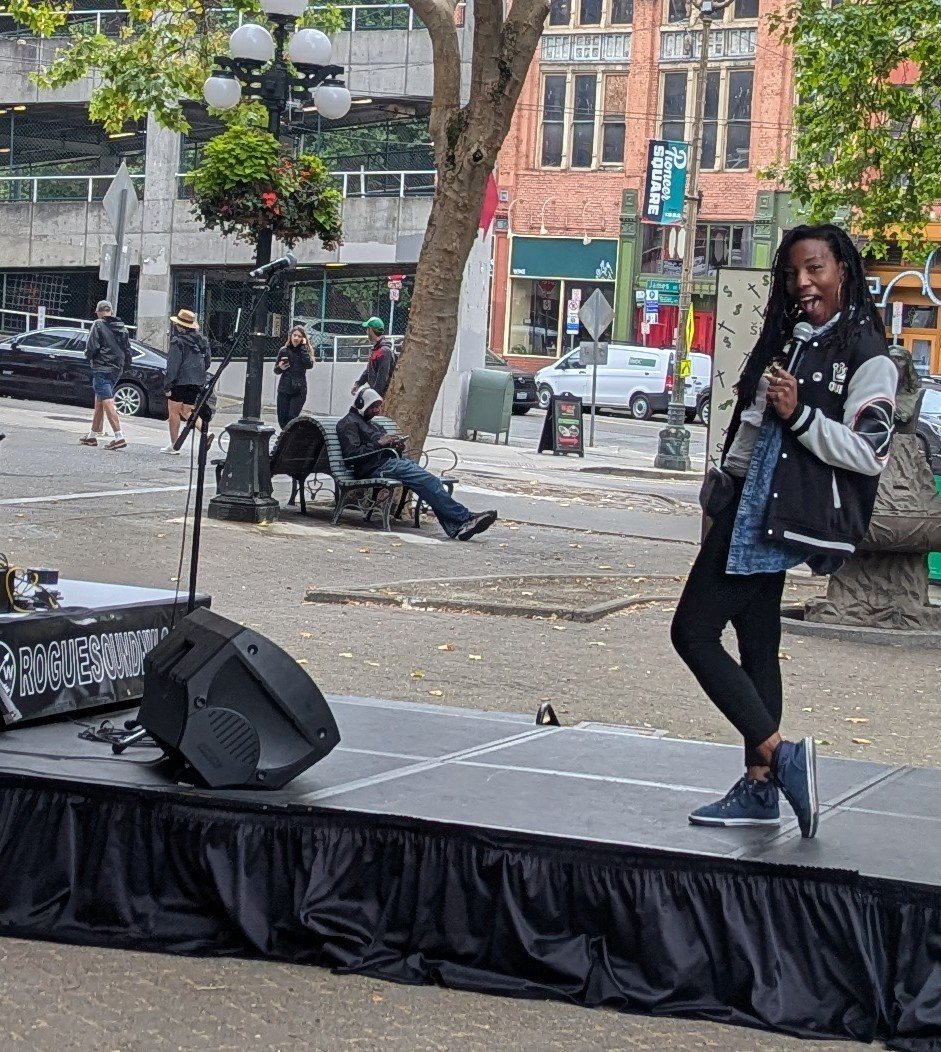 A comedian on stage in Pioneer Square, Seattle, during Downtown Seattle Association's Lunch and Laughs summer program.