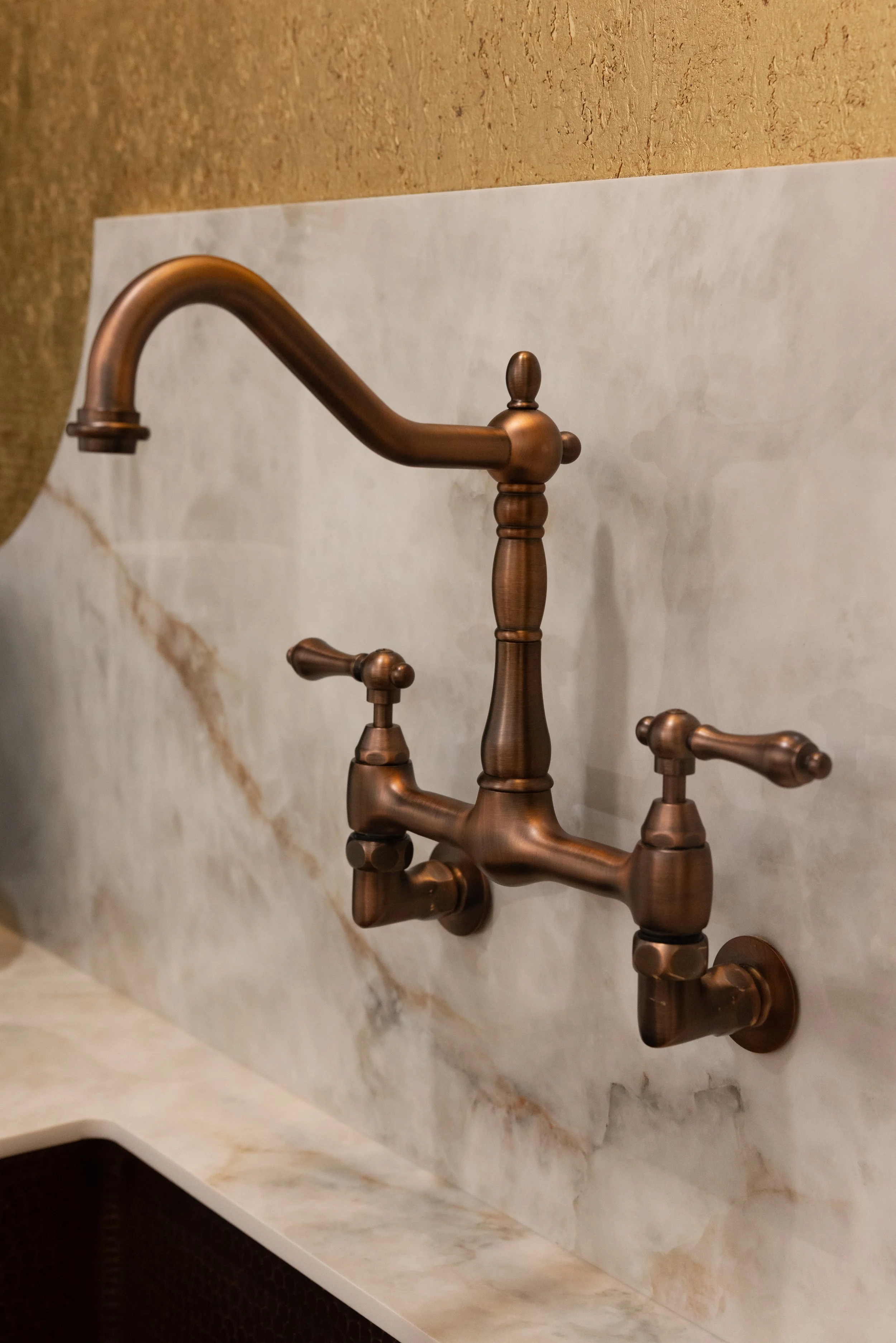 Close-up of vintage bronze bathroom faucet mounted on light marble backsplash with a dark textured wall below.