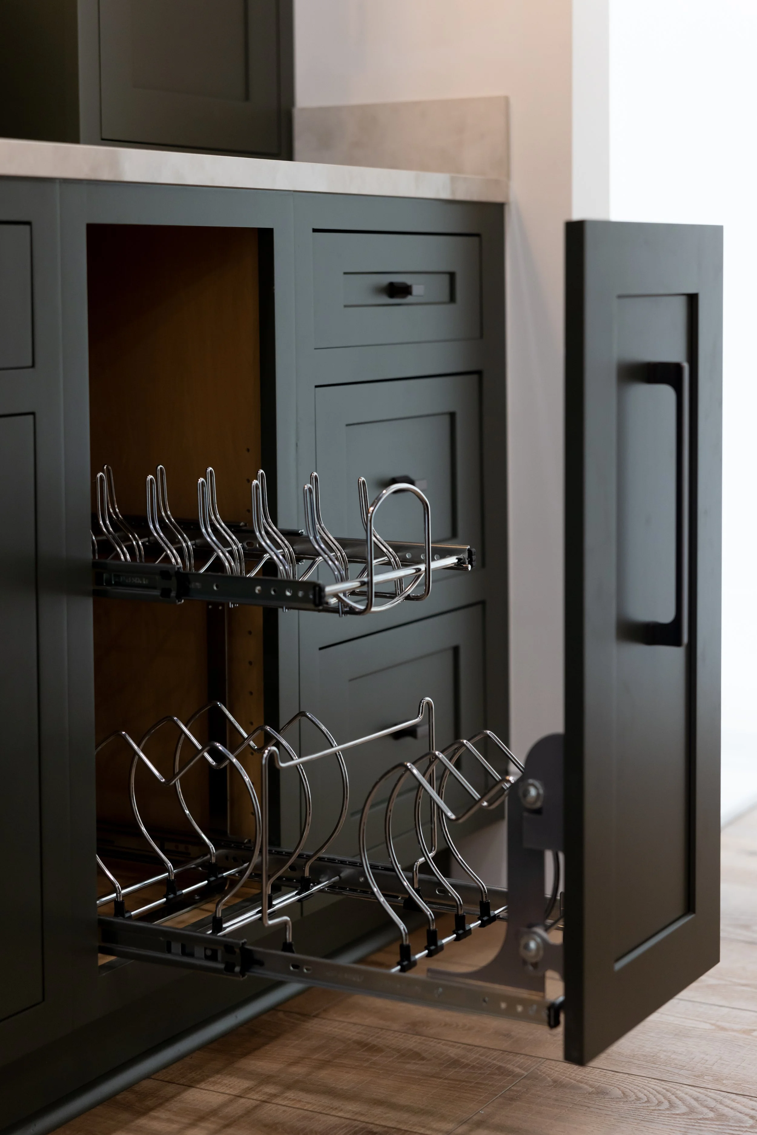 Close-up of an open dishwasher with empty racks, showing metallicware holders inside a gray kitchen cabinet.