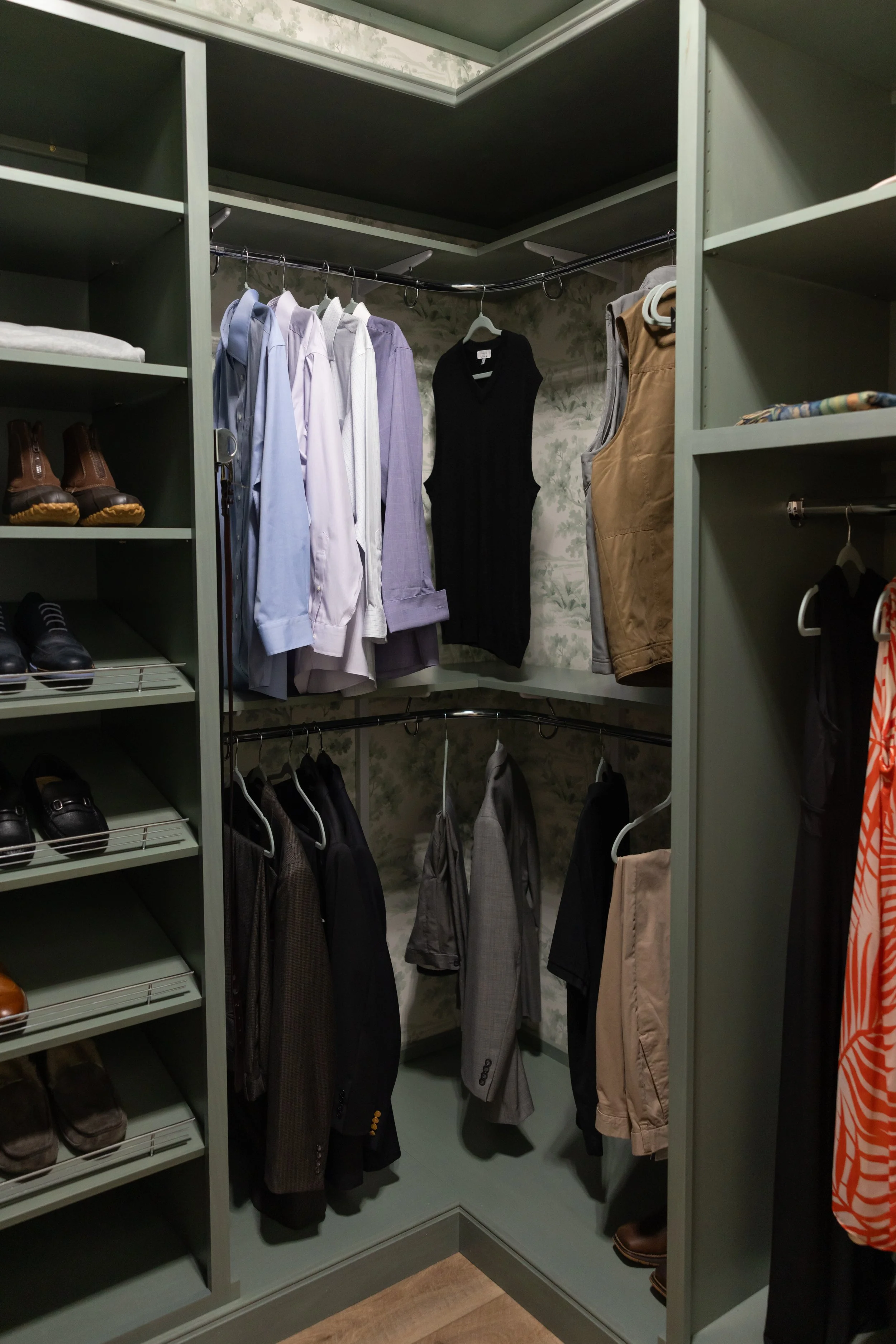 A walk-in closet with shelves, hanging racks, and shoes neatly organized. Various clothing items such as shirts, jackets, and trousers are hanging or folded on the shelves.