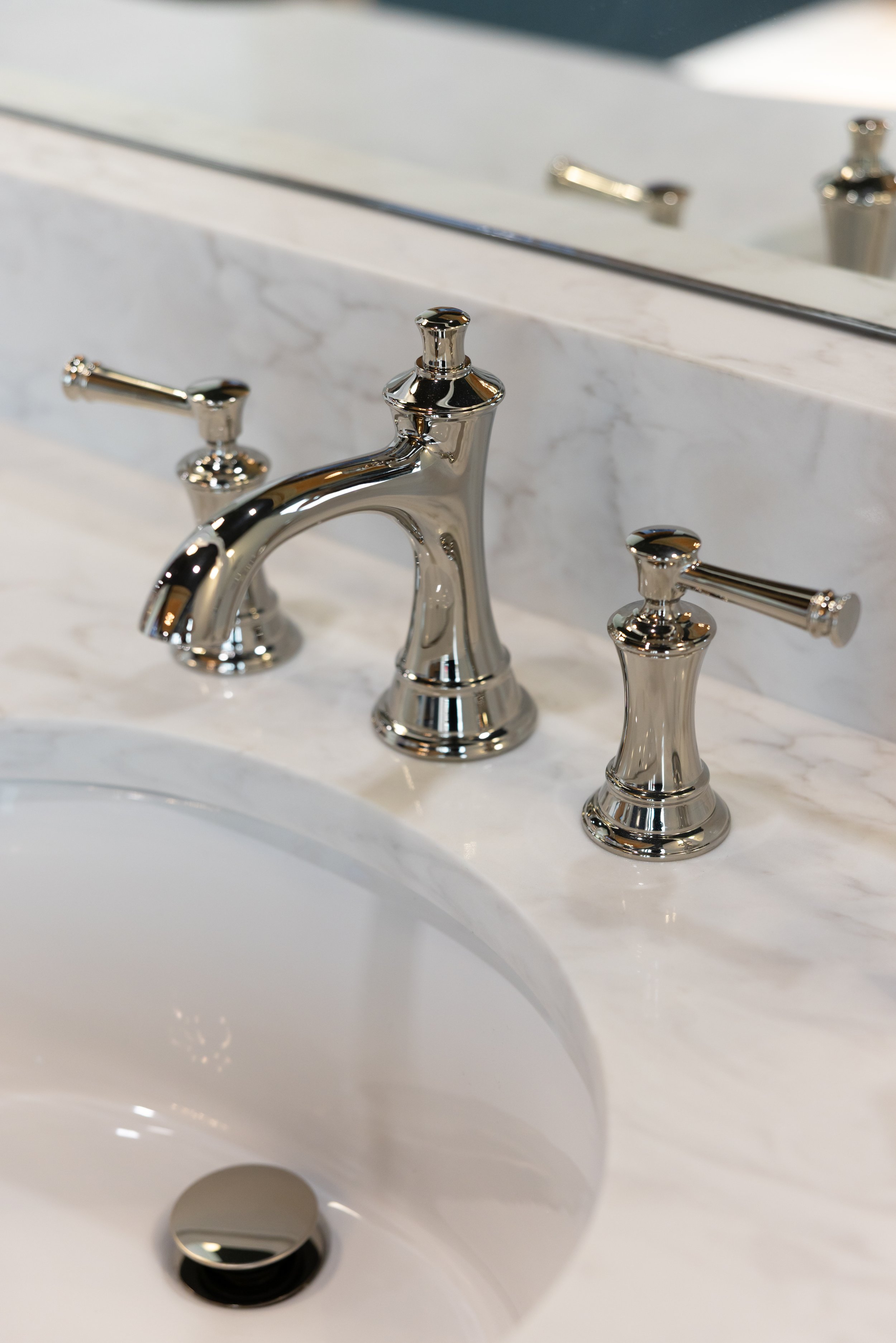 Close-up of a chrome faucet with separate hot and cold water handles on a white marble bathroom sink with a mirror in the background.