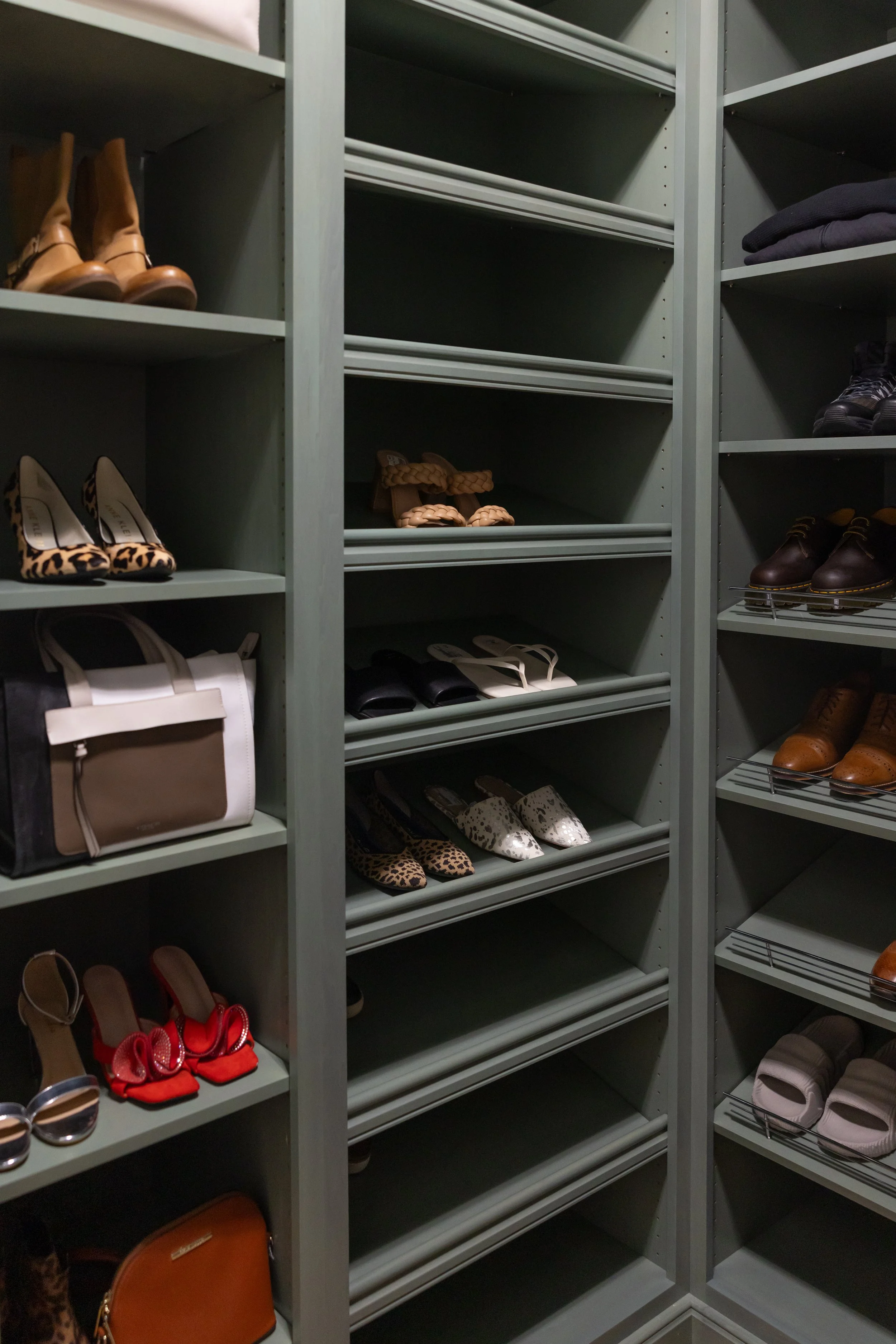 Shelves in a walk-in closet with various shoes including heels, boots, sandals, and sneakers, many of which are empty or on the floor.