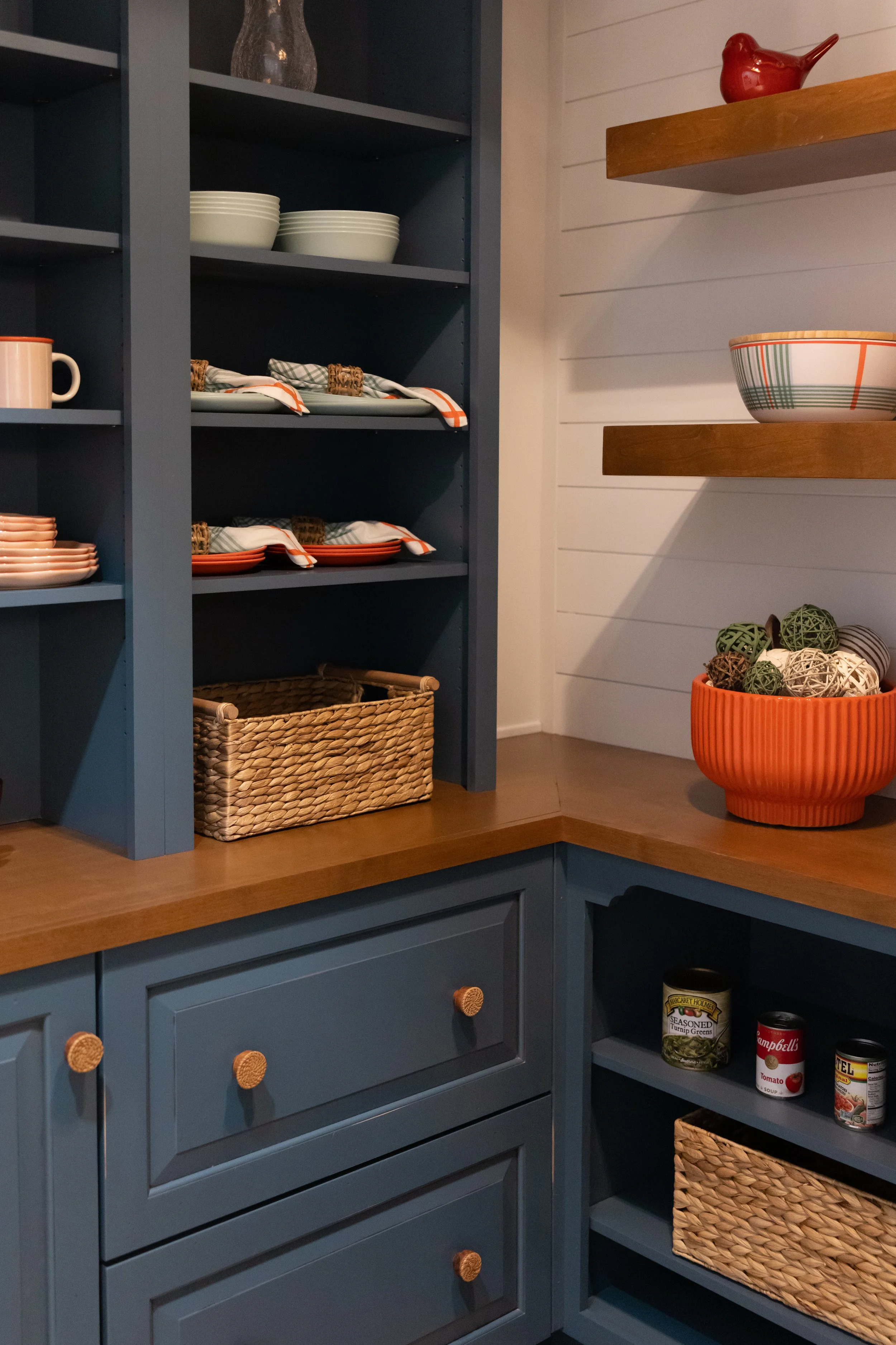 Kitchen shelving with stacked bowls, a mug, and decorative baskets and balls, painted in blue with wooden accents.