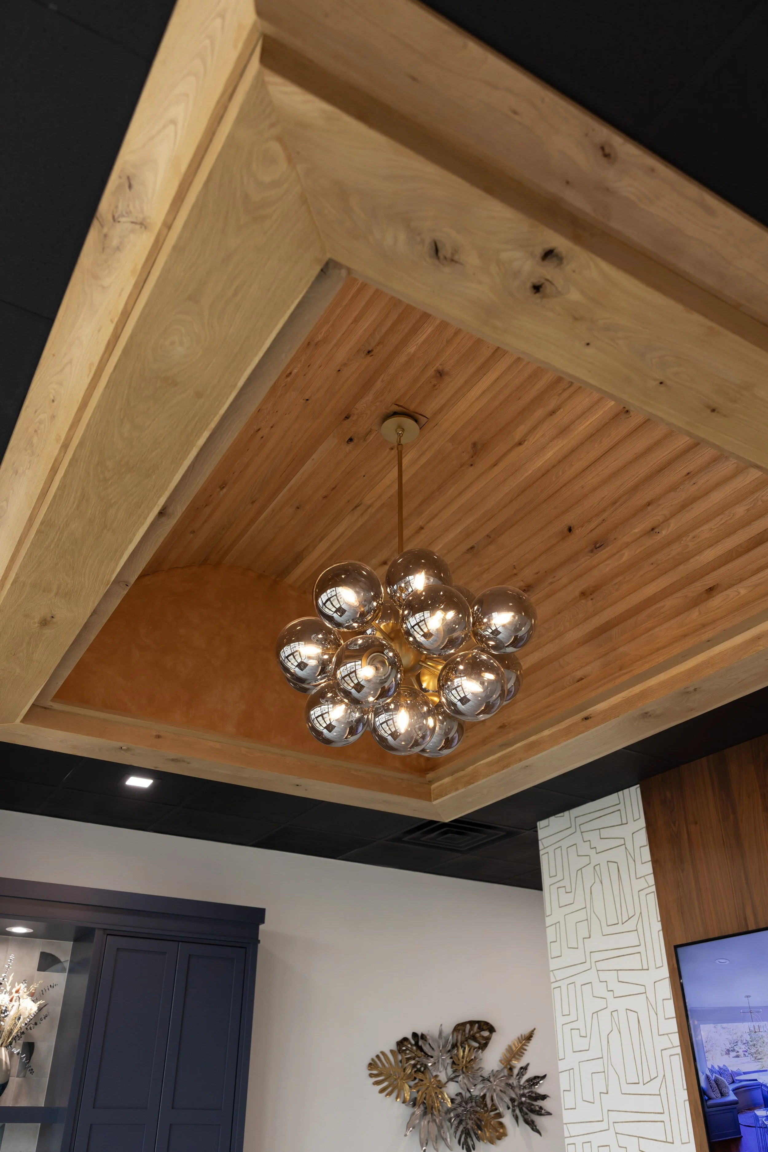 Ceiling with wooden panels, modern chandelier with spherical glass bulbs, and decorative wall art with metallic leaves.