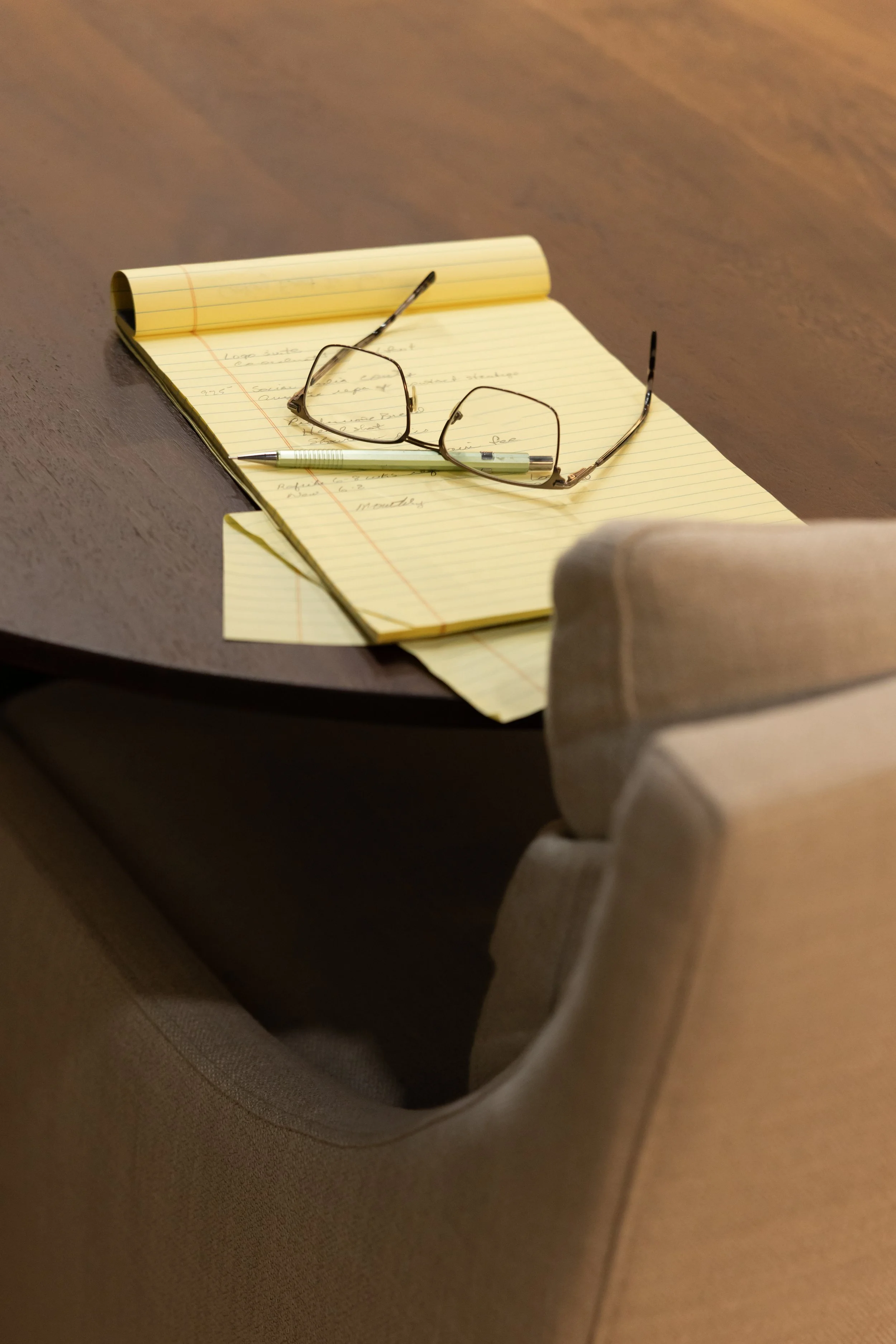 A notebook with handwritten notes, a pen, and a pair of glasses resting on it on an airplane tray table.