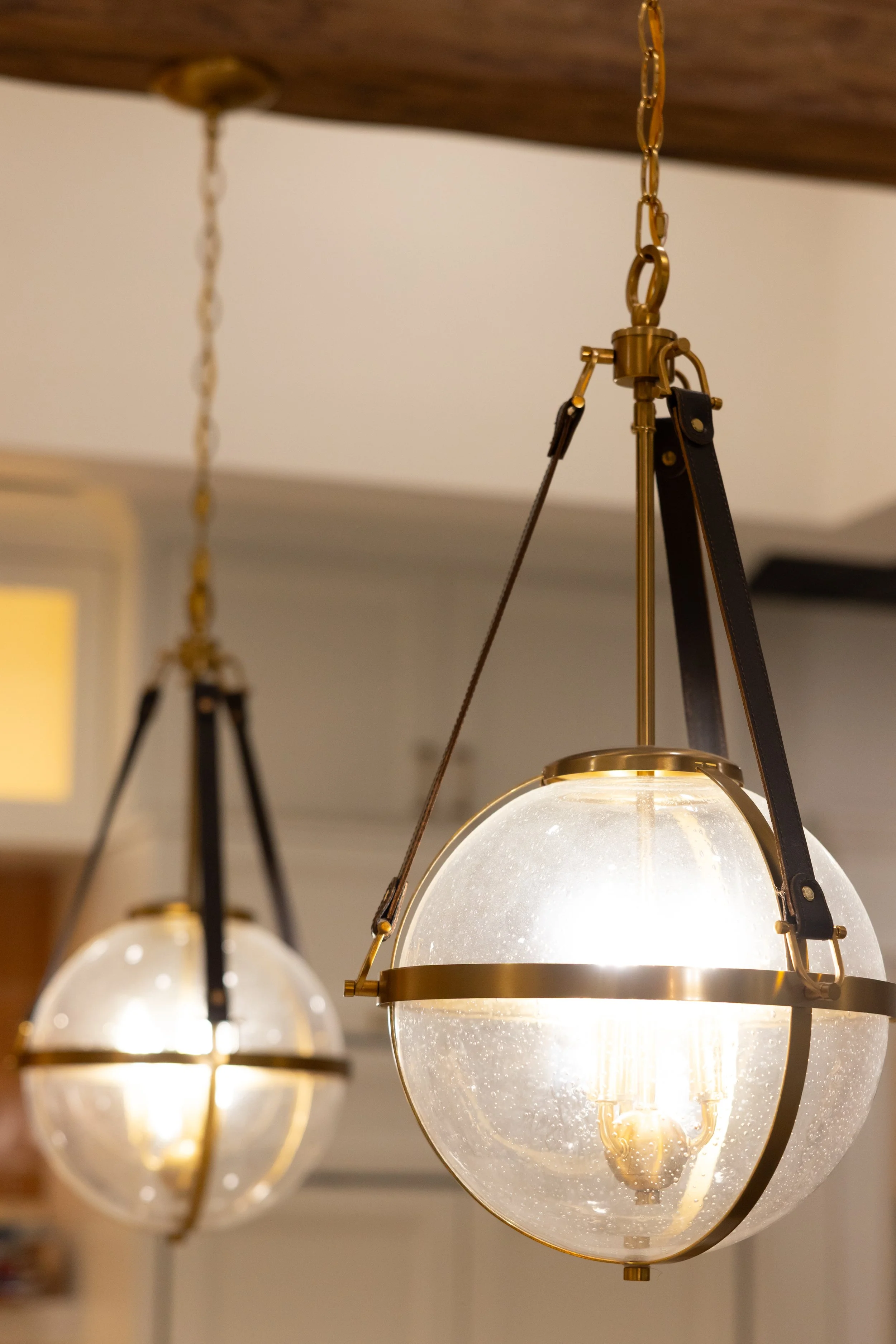 Close-up of hanging vintage pendant lights with glass globes, metal accents, and warm glowing bulbs, attached by chains from a wooden ceiling.