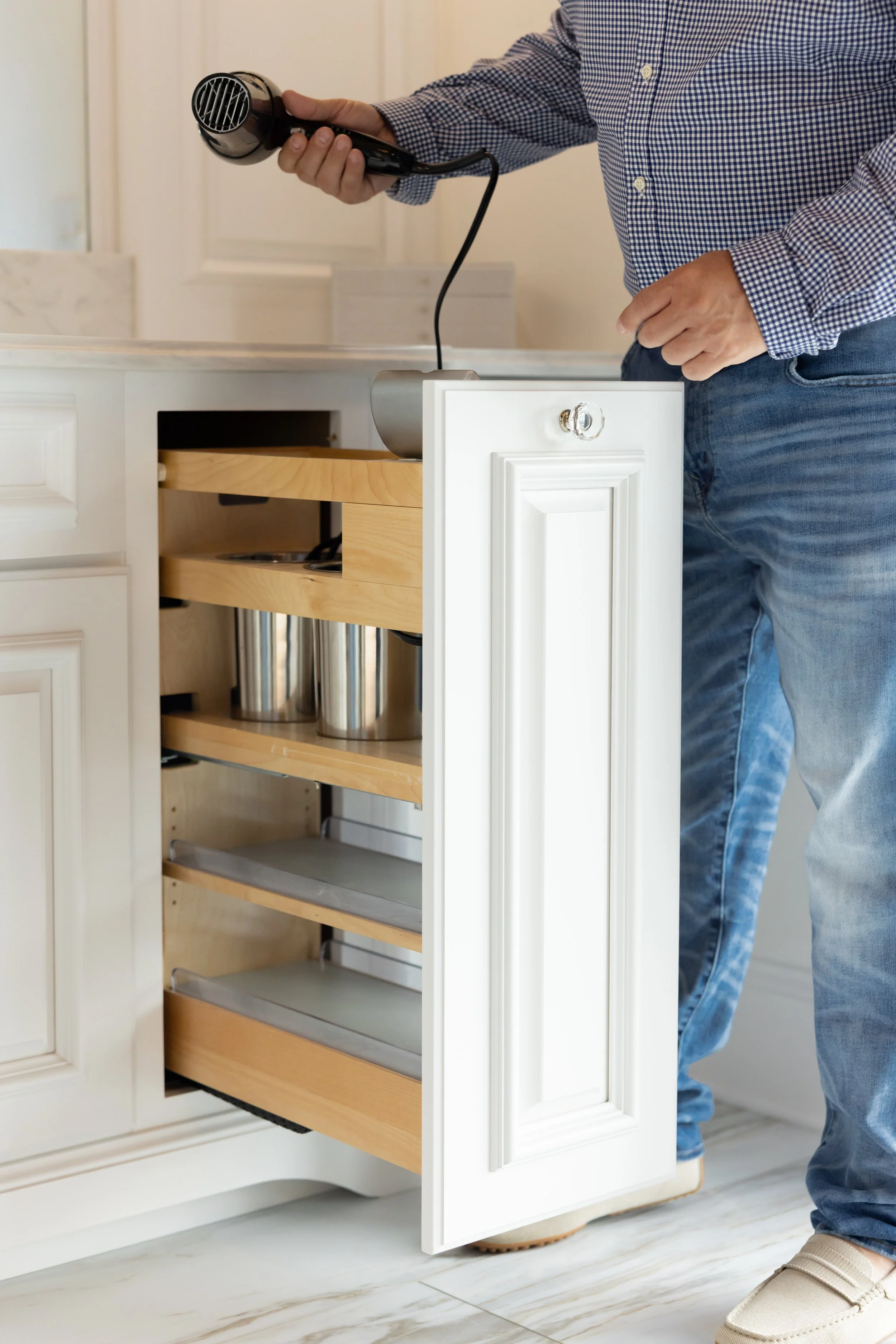 Person opening a kitchen cabinet with a black handheld hairdryer.