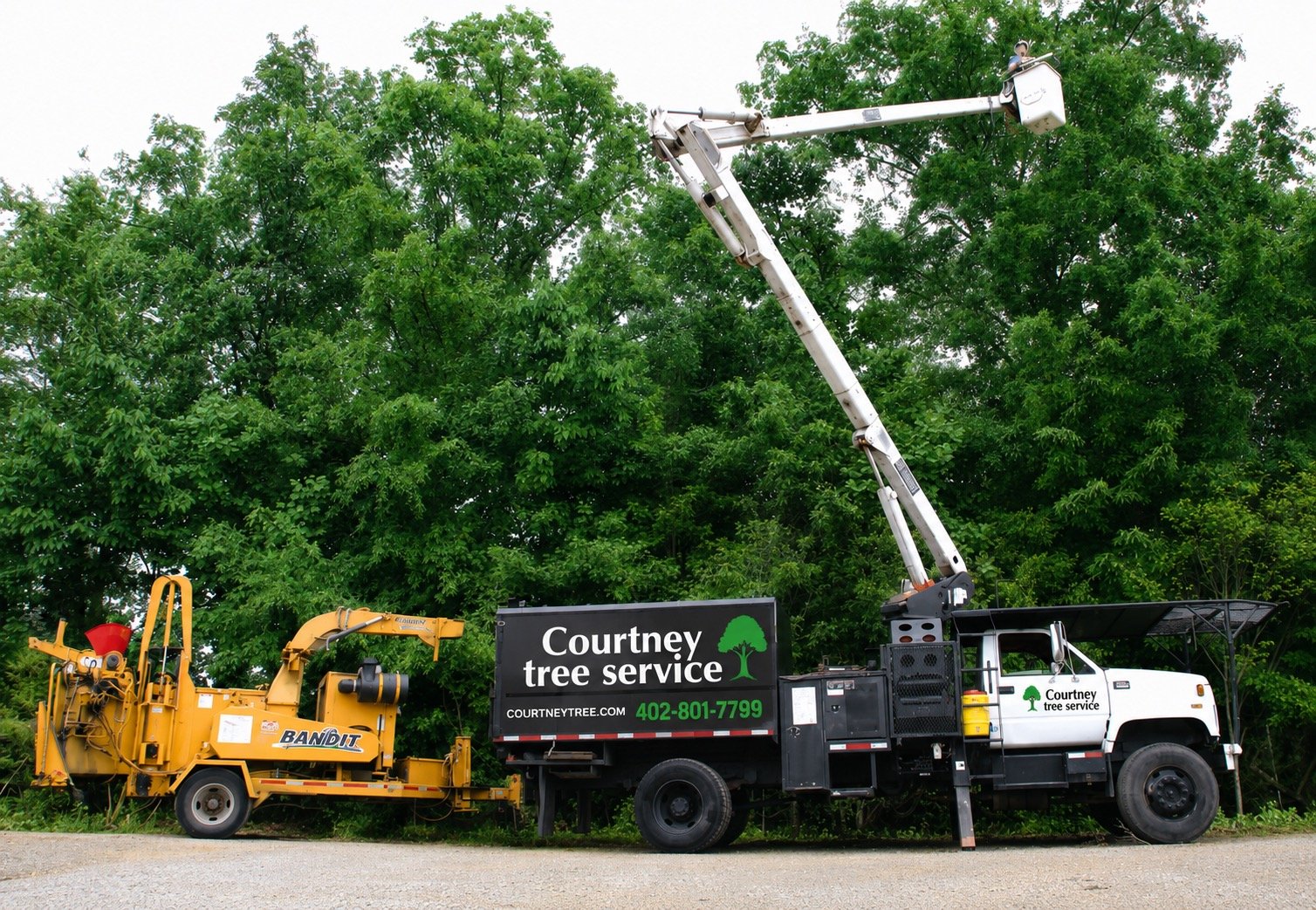 Tree service truck with an elevated bucket and a trailer with equipment, parked on a road in front of green trees. The truck has branding for Courtney Tree Service, including a website and phone number.