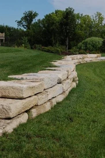 Stone retaining wall with green grass and trees in the background.