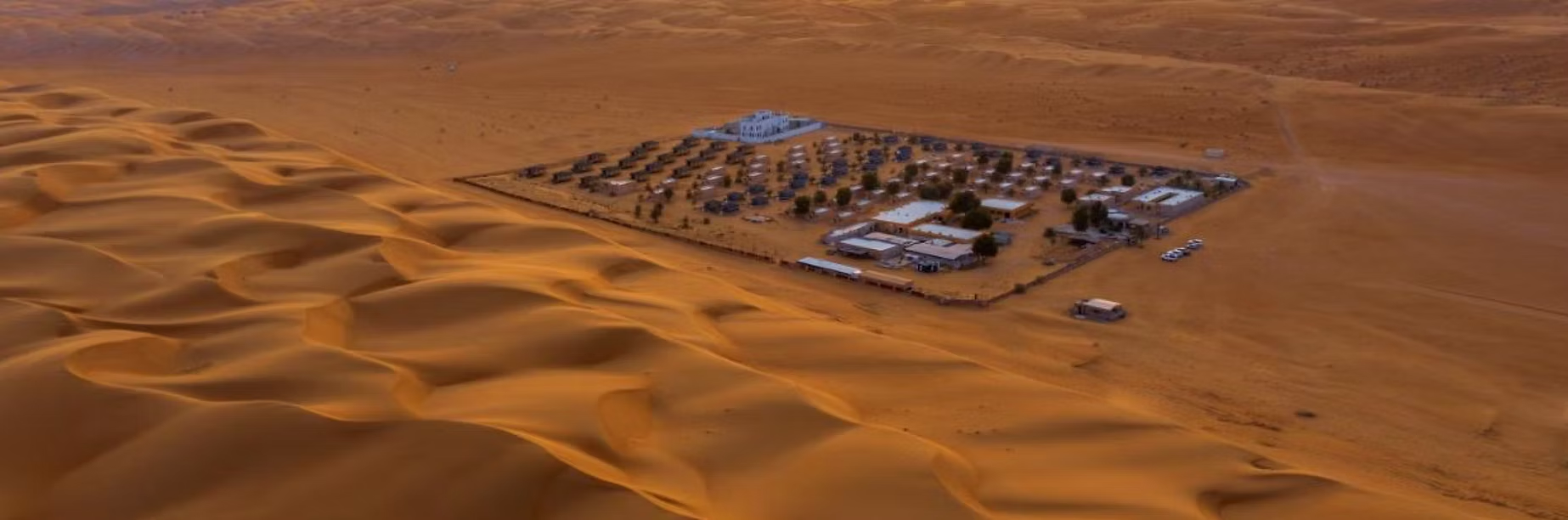 Vue aérienne d'un campement ou d'une station dans un désert avec des dunes de sable doré.