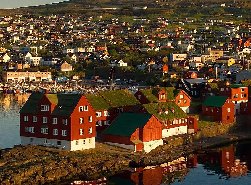 Villages colorés avec maisons en bois rouges et verts, côtes rocheuses, marina avec bateaux, dans une région vallonnée au coucher du soleil.