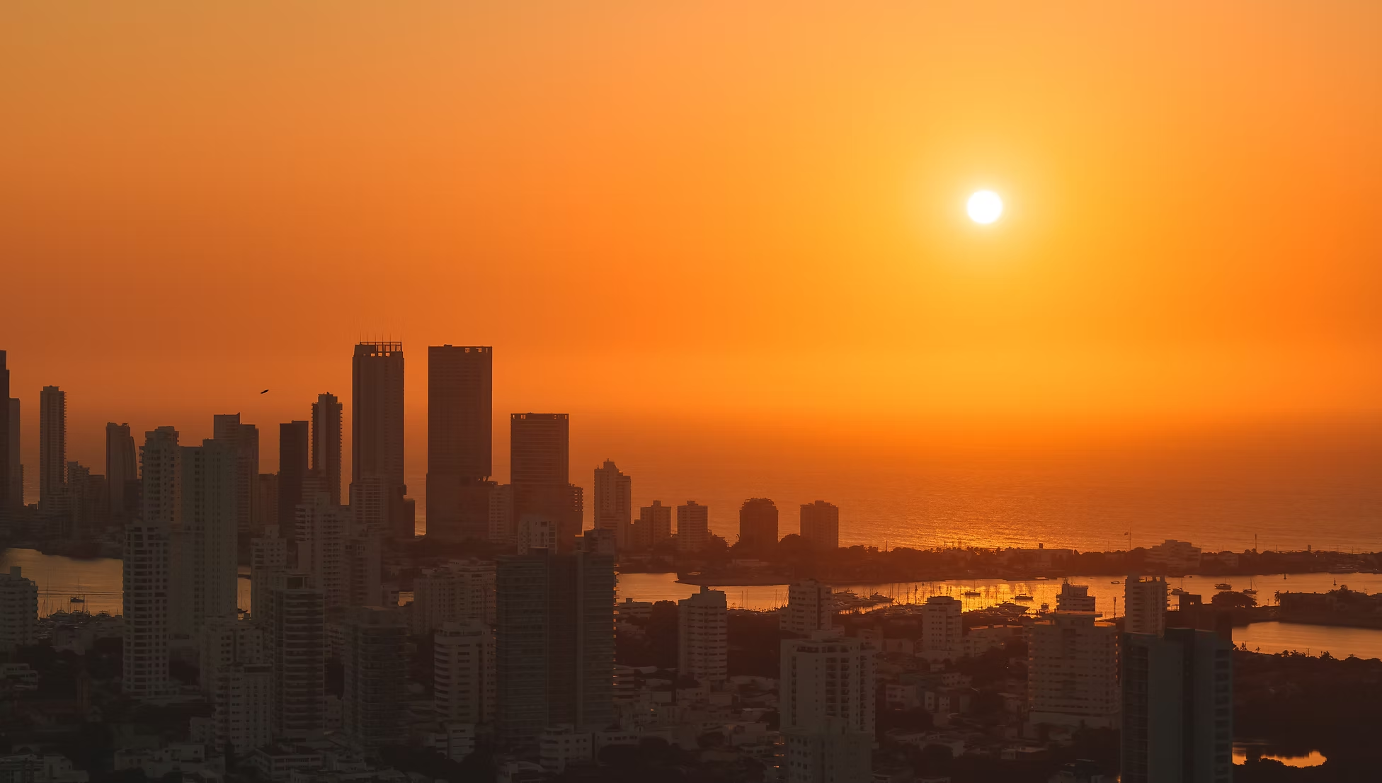 Coucher de soleil au dessus d'une ville avec plusieurs gratte-ciel au bord de la mer.