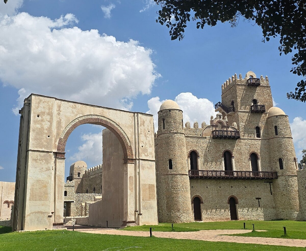 Château médiéval avec tours et murailles, entrée en pierre ancienne, ciel bleu avec quelques nuages.