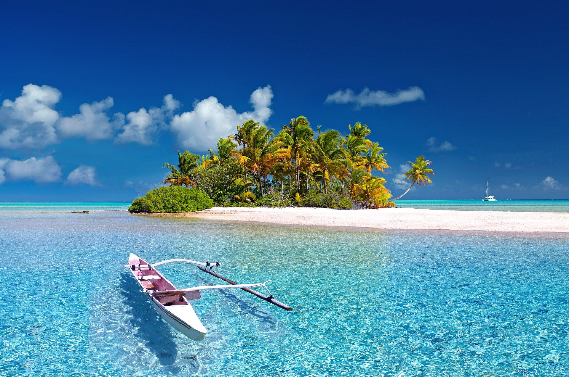 Une petite île tropicale avec des palmiers, une plage de sable blanc, et l'océan turquoise, avec un voilier au loin.