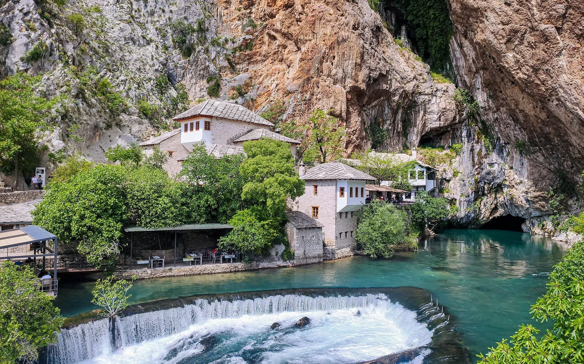 Maisons blanches construits dans une grotte au bord d'une rivière turquoise entourée de falaises rocheuses vertes et brossées.