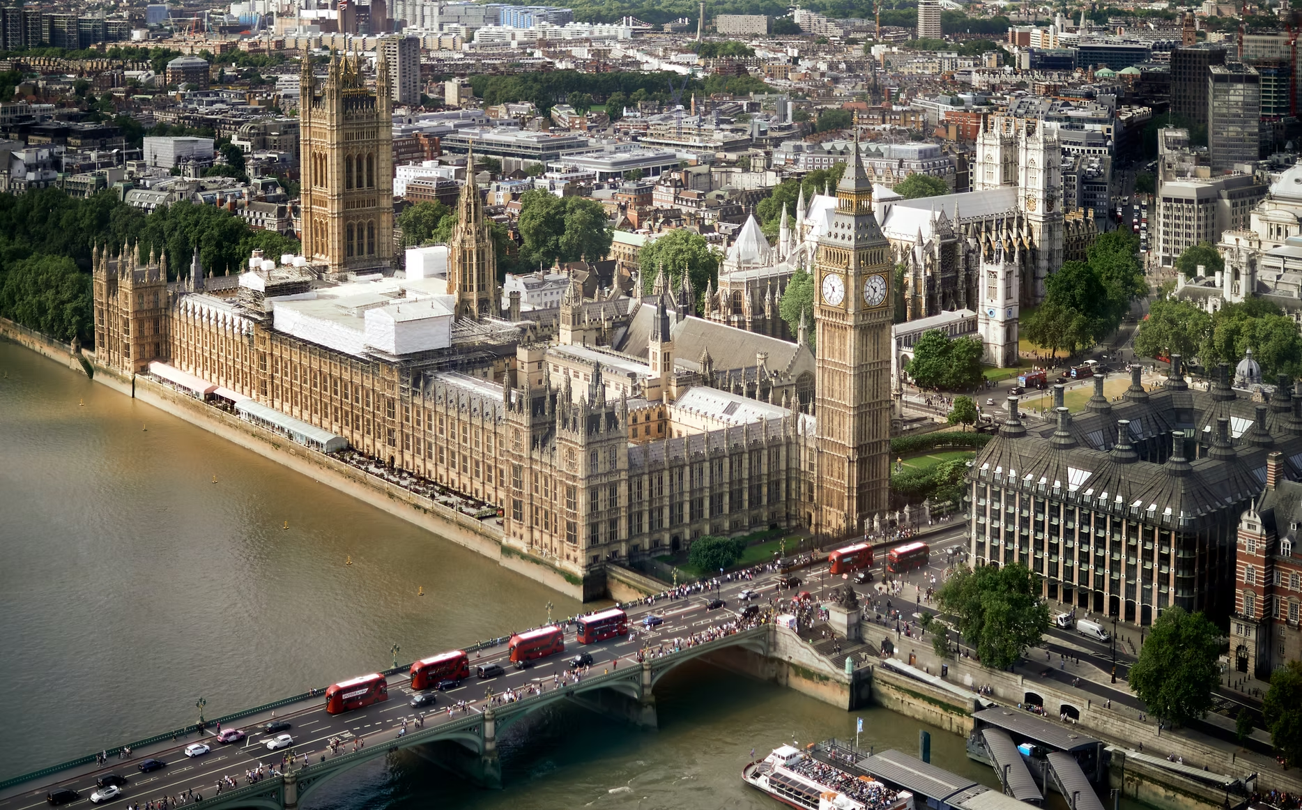 Vue aérienne du Palais de Westminster avec Big Ben à Londres, en bordure de la Tamise, avec des bus rouges, piétons et un pont. Ville moderne en arrière-plan.
