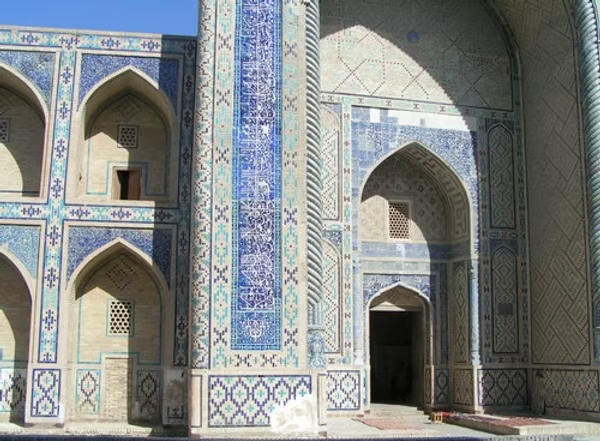 Une façade ornée avec des motifs en mosaïque bleue et blanche, avec des arches et des fenêtres en forme d'arc, probablement un bâtiment historique ou religieux en architecture islamique.