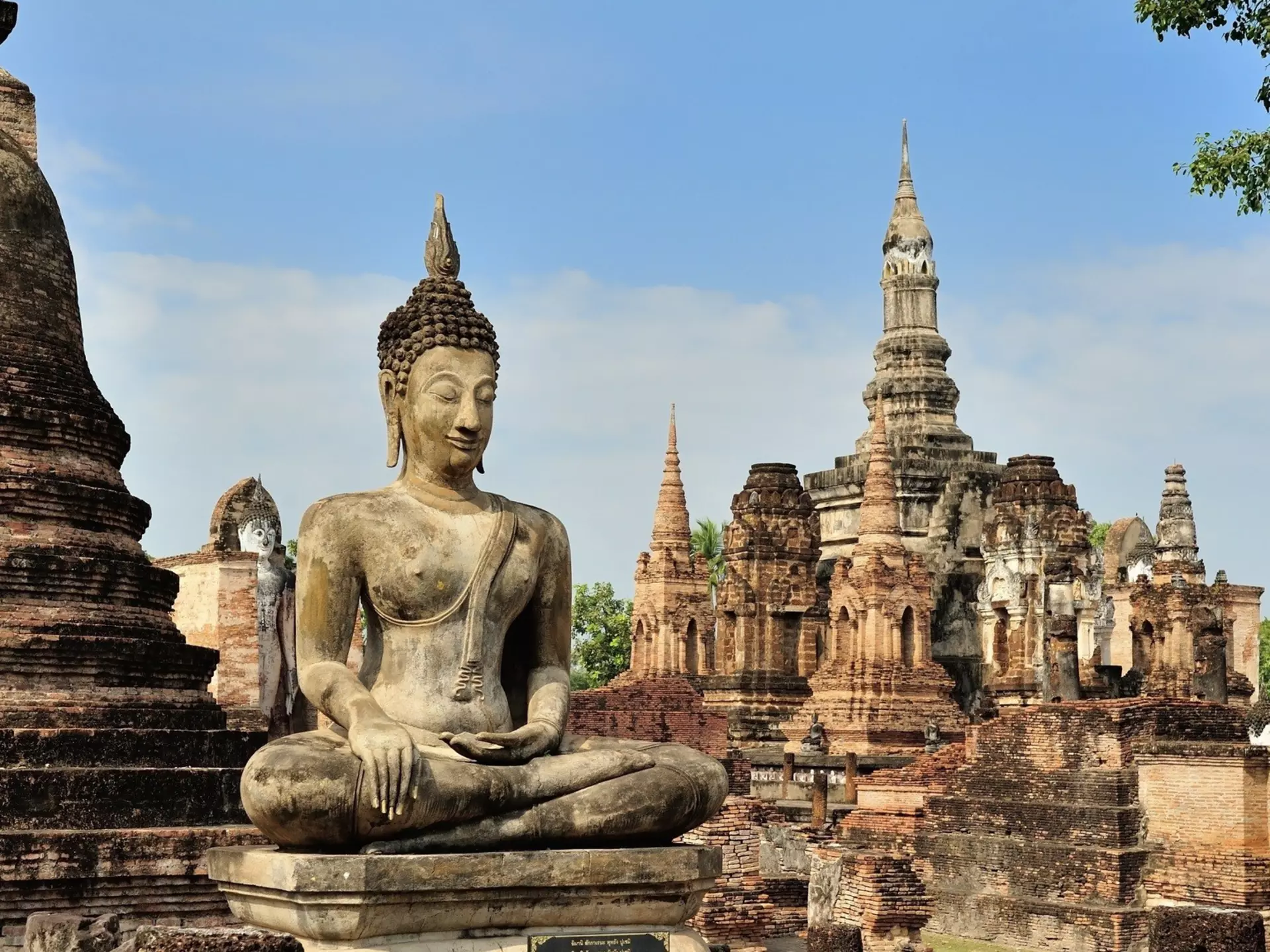 Statue de Bouddha assis devant un ancien site d'architecture historique en pierre avec des tours et des structures en ruines.
