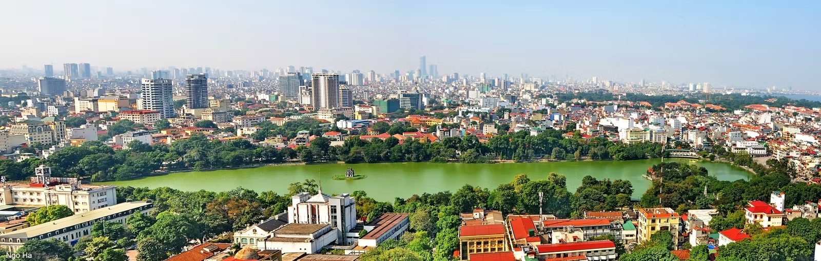 Vue panoramique d'une ville urbaine avec un grand parc central et un lac, entourée de bâtiments modernes et de nombreux arbres.