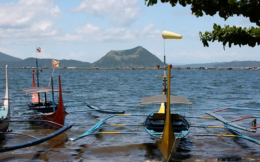 Plusieurs bateaux traditionnels avec voiles amarrés dans un lac, avec une île en arrière-plan, sous un ciel partiellement nuageux.