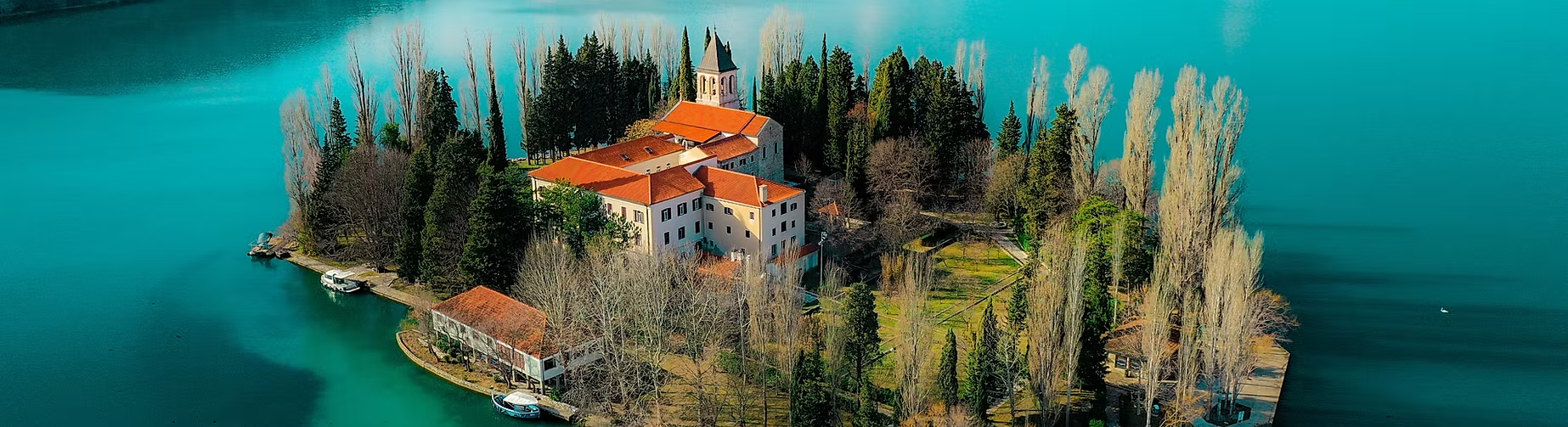 Île au centre d'un lac avec un bâtiment religieux et des maisons entourées d'arbres, vue aérienne