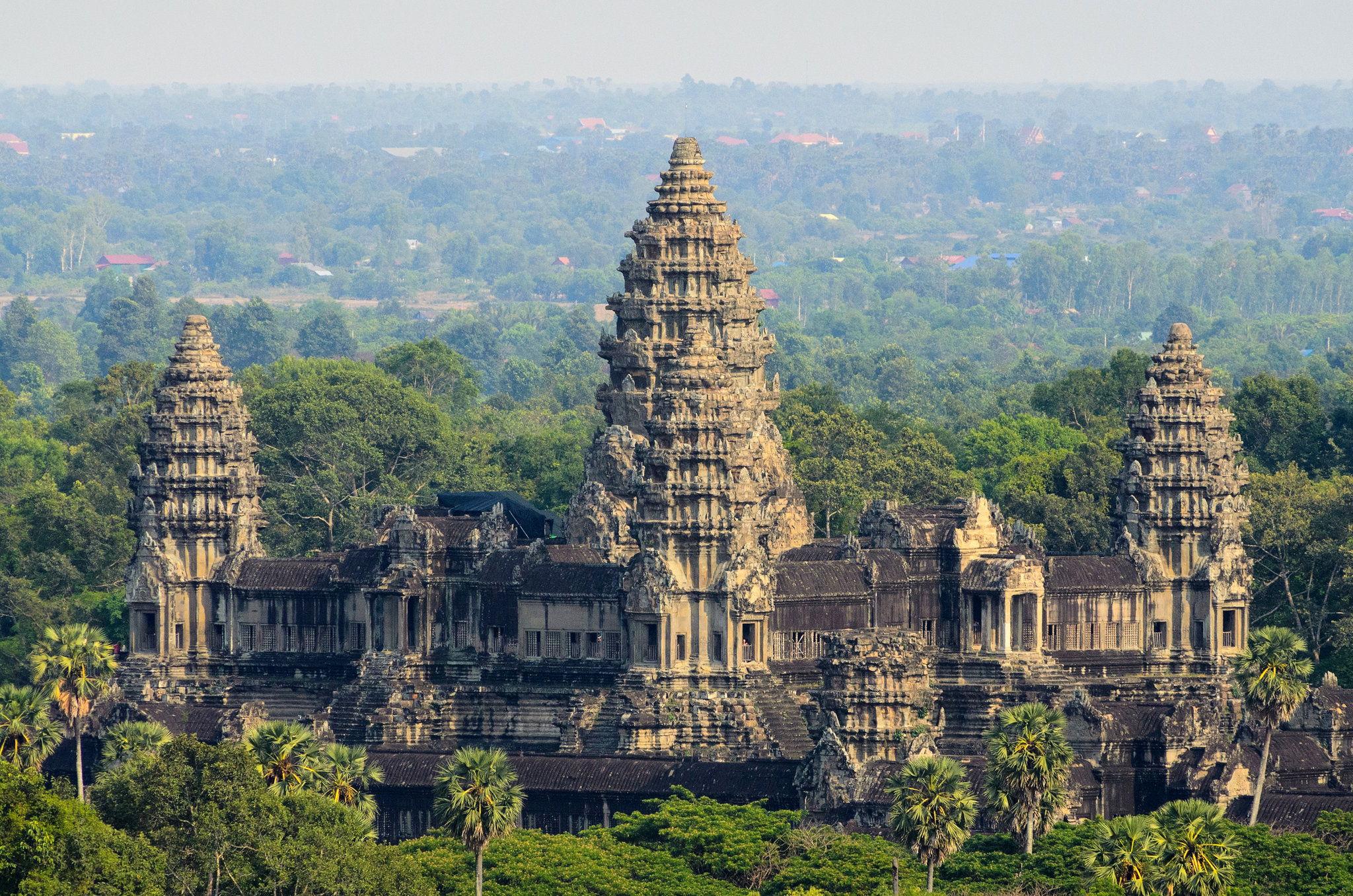 Vue d'ensemble des temples d'Angkor Wat avec des tours en pierre et une végétation luxuriante, fond flou de la forêt et du ciel.