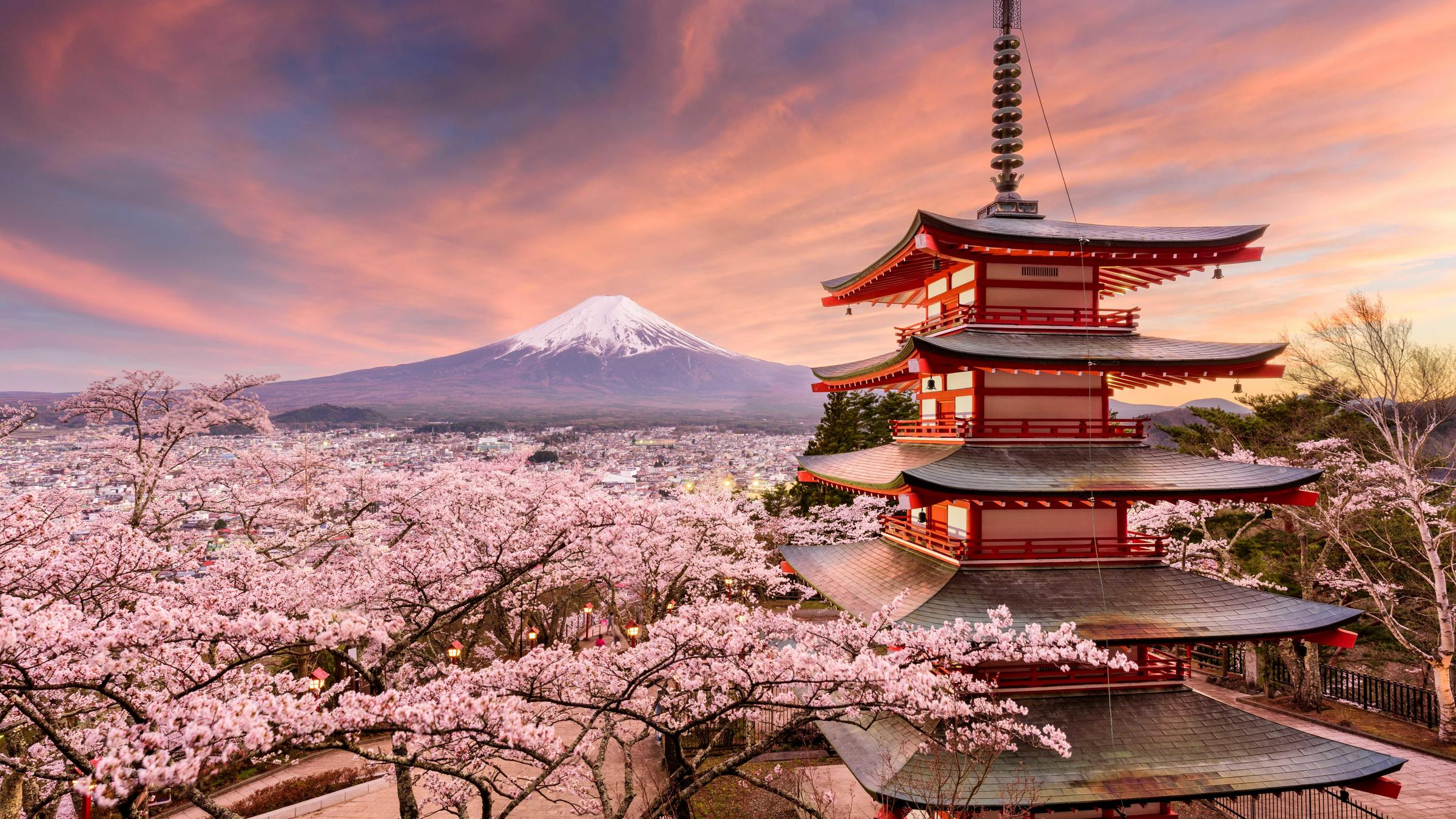 Vue panoramique du mont Fuji enneigé, avec un temple japonais traditionnel rouge et vert au premier plan, entouré d'arbres verts.