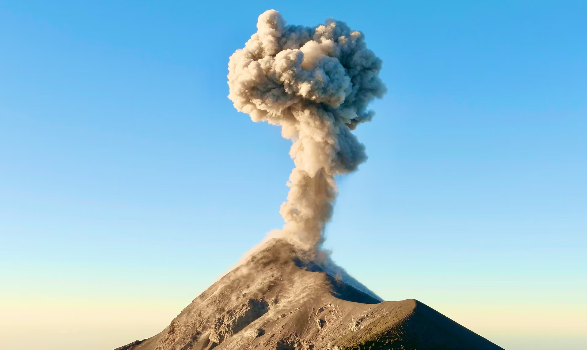 Une éruption volcanique avec une colonne de fumée s'élevant dans le ciel bleu.