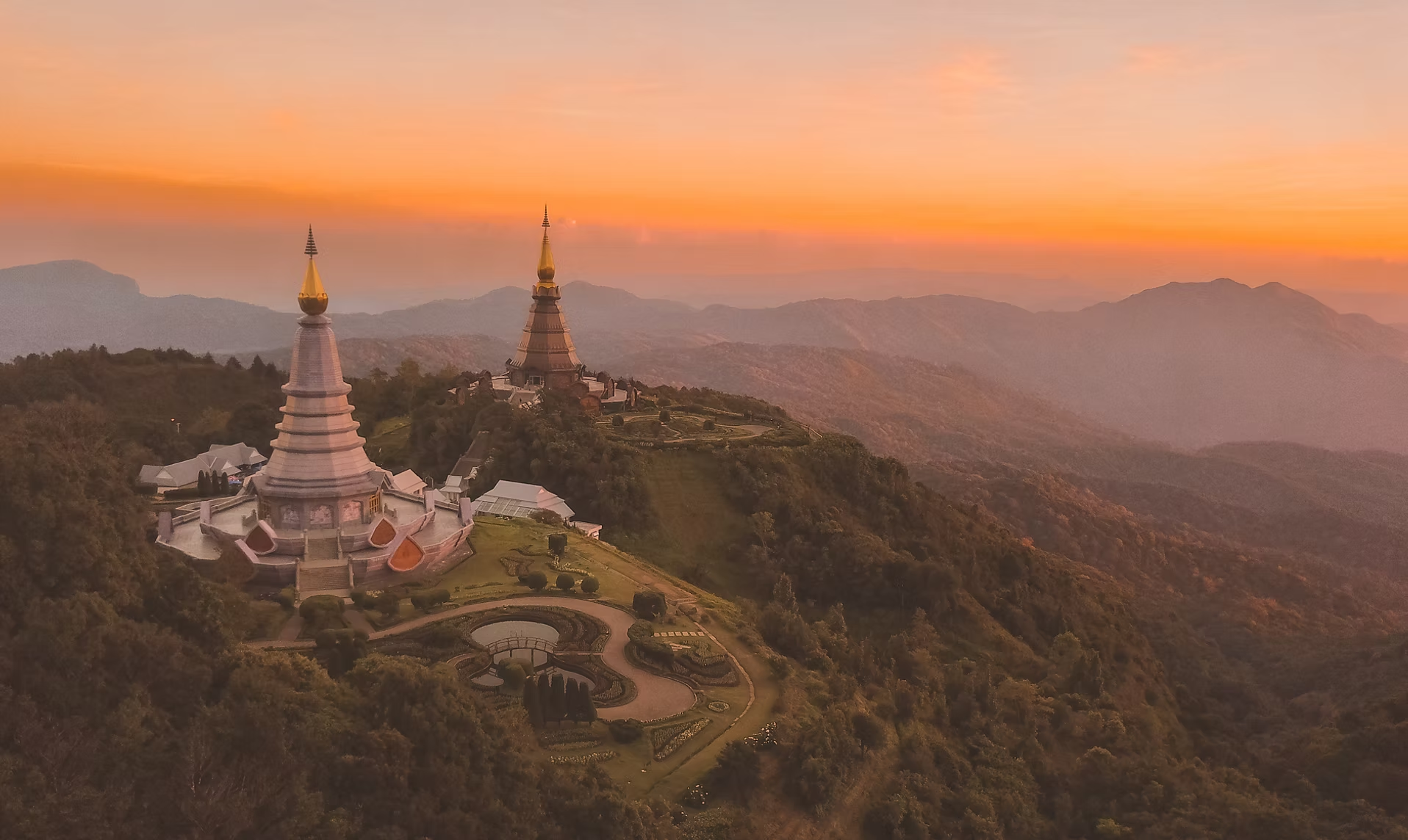 Temples bouddhistes avec des toits dorés sur une colline, au coucher du soleil, avec une vue sur des montagnes environnantes.