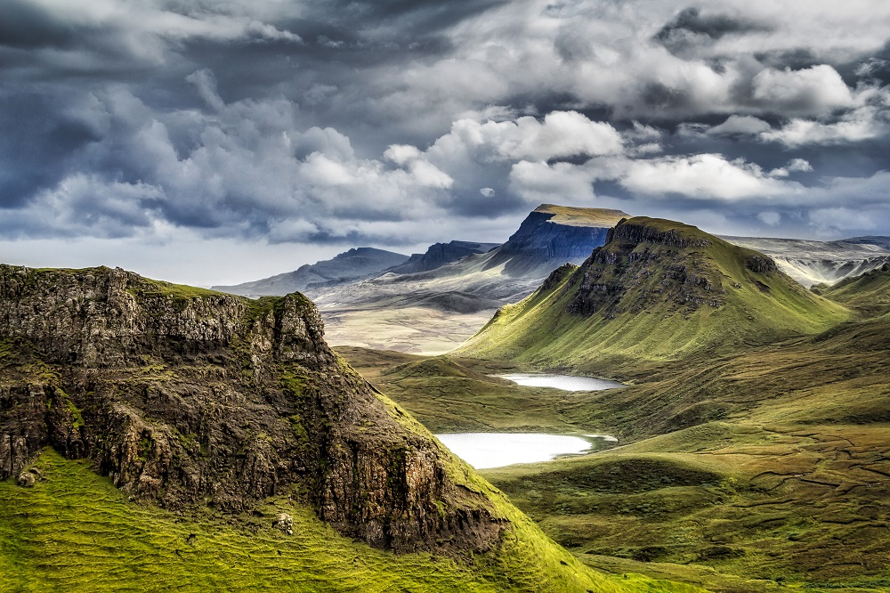 Paysage montagneux avec des collines verdoyantes, des lacs, et un ciel nuageux.