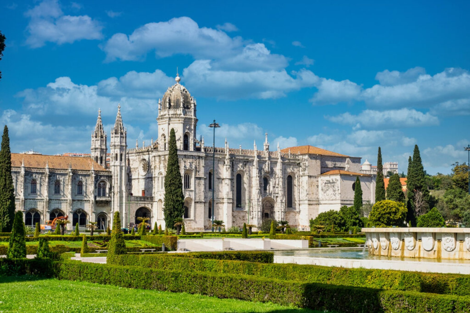 Vue d'un ancien bâtiment religieux ou historique avec un parc jardin devant, ciel bleu avec quelques nuages.