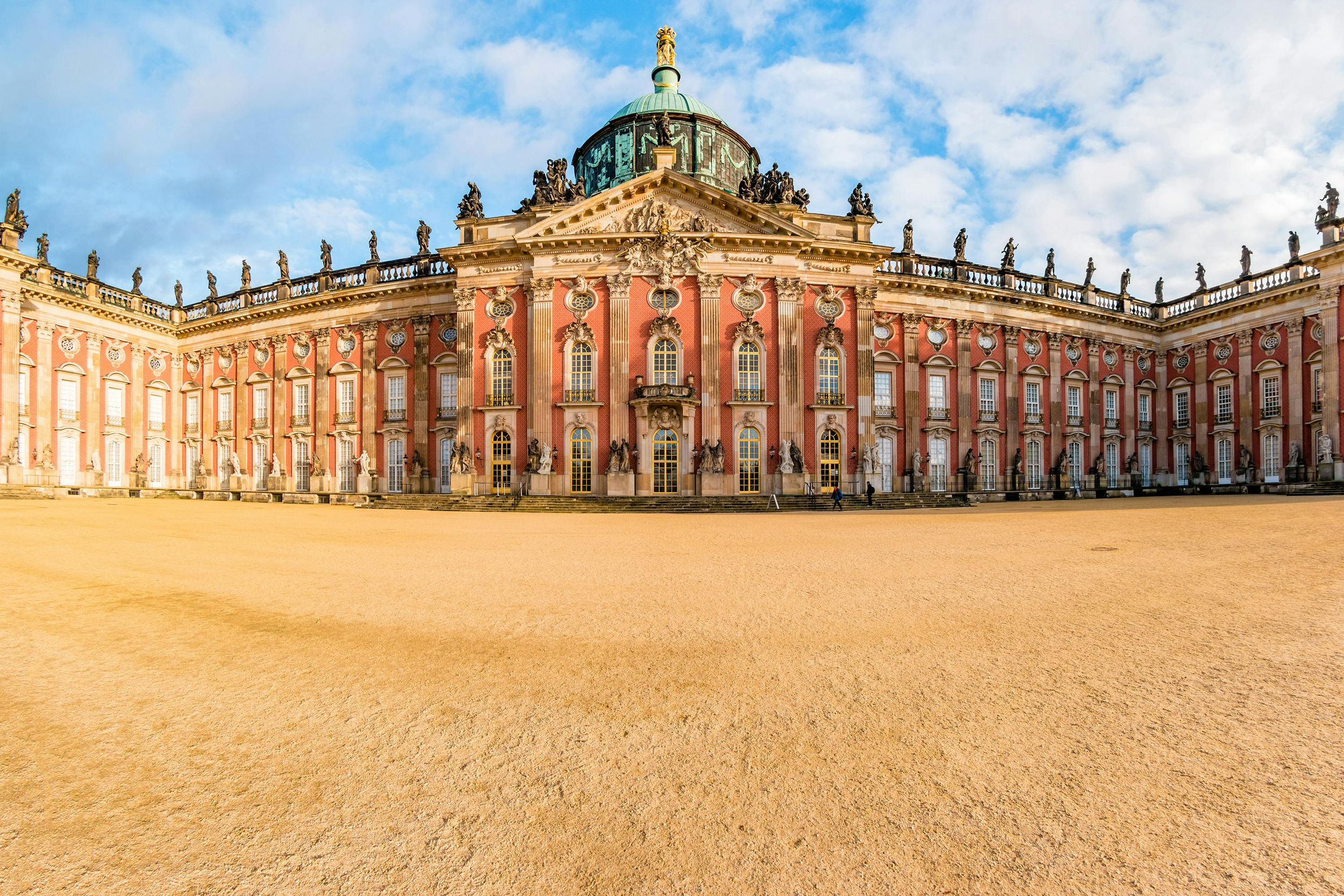 Vue d'un bâtiment historique de style baroque avec des statues décoratives et des fenêtres ornées, sur un fond de ciel bleu avec quelques nuages.